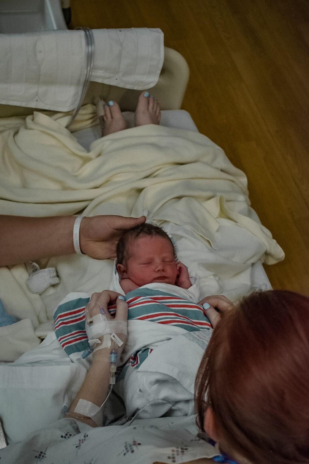 Newborn baby wrapped in striped outfit being examined in hospital setting.