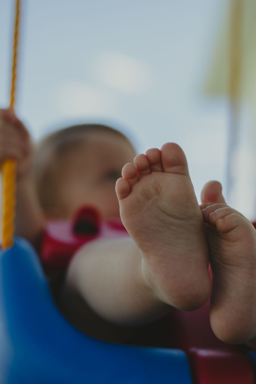Small bare feet peek out from a red toy car against a light background.