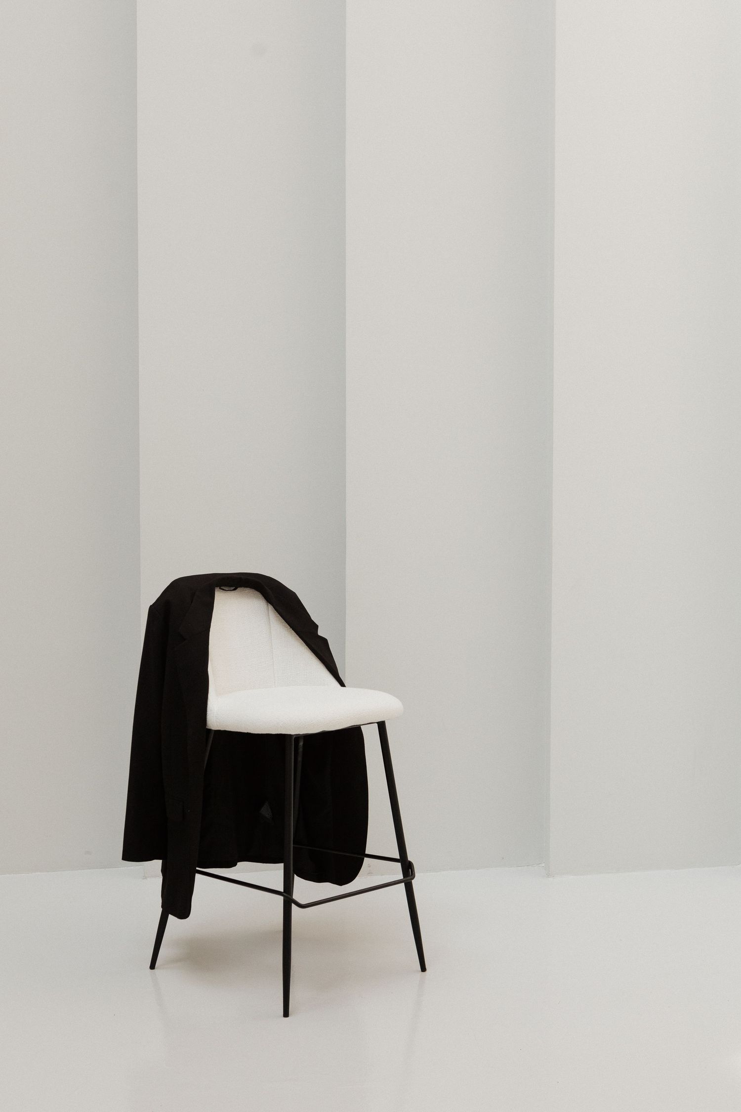 Minimalist art series showing a black jacket draped over white chairs against a stark white background.