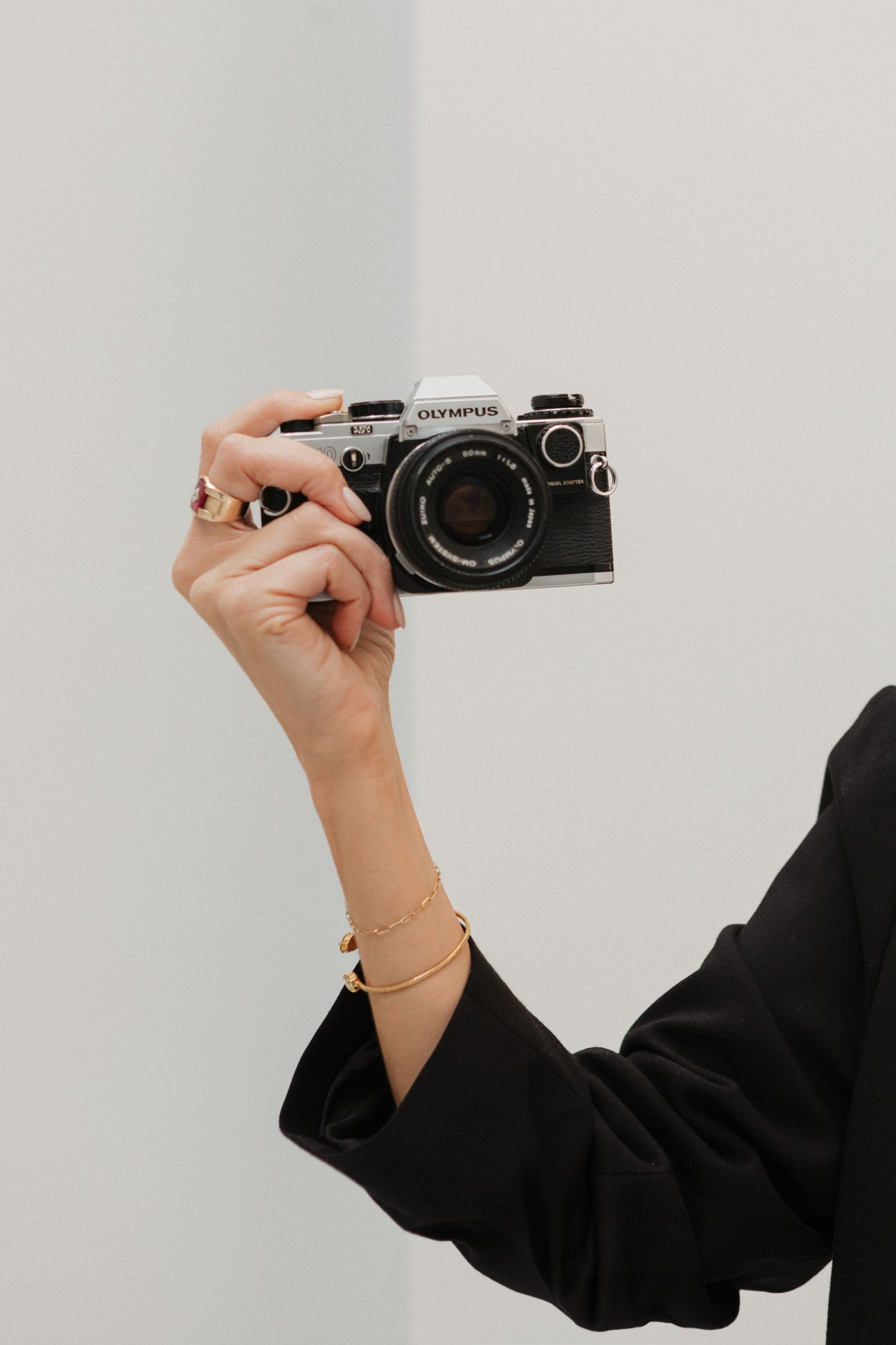 Hand in black sleeve holds vintage Olympus camera against white background.
