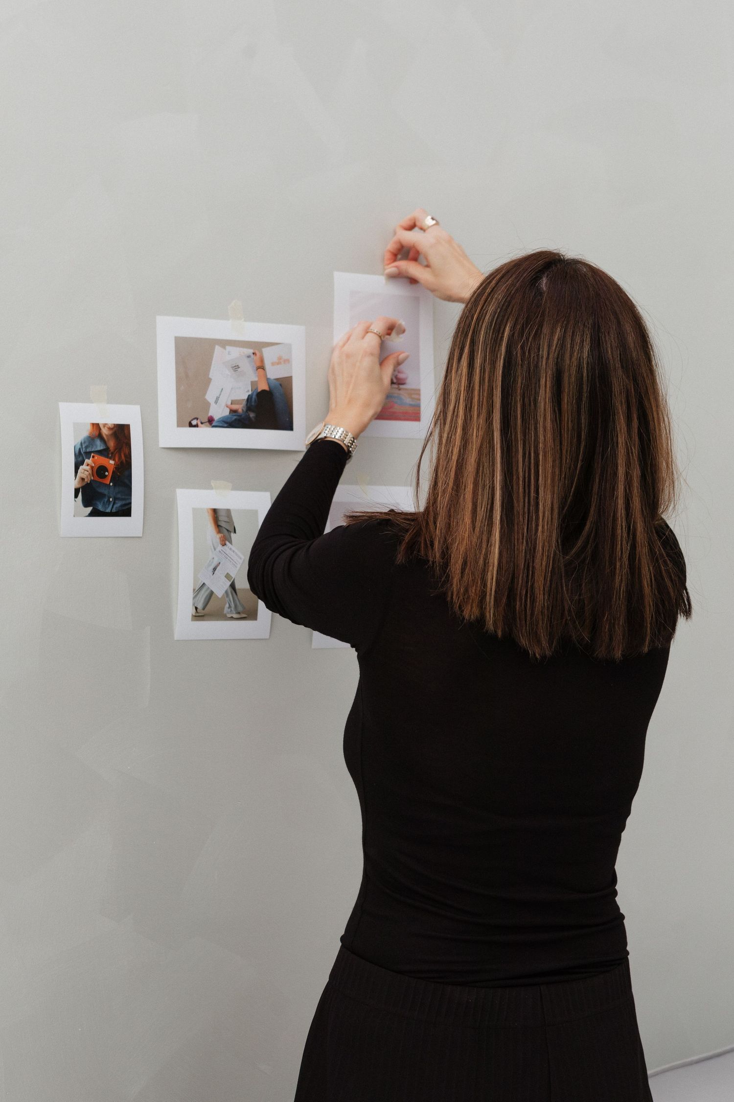 Person in black attire hanging photographs on a white wall in a gallery-style display.