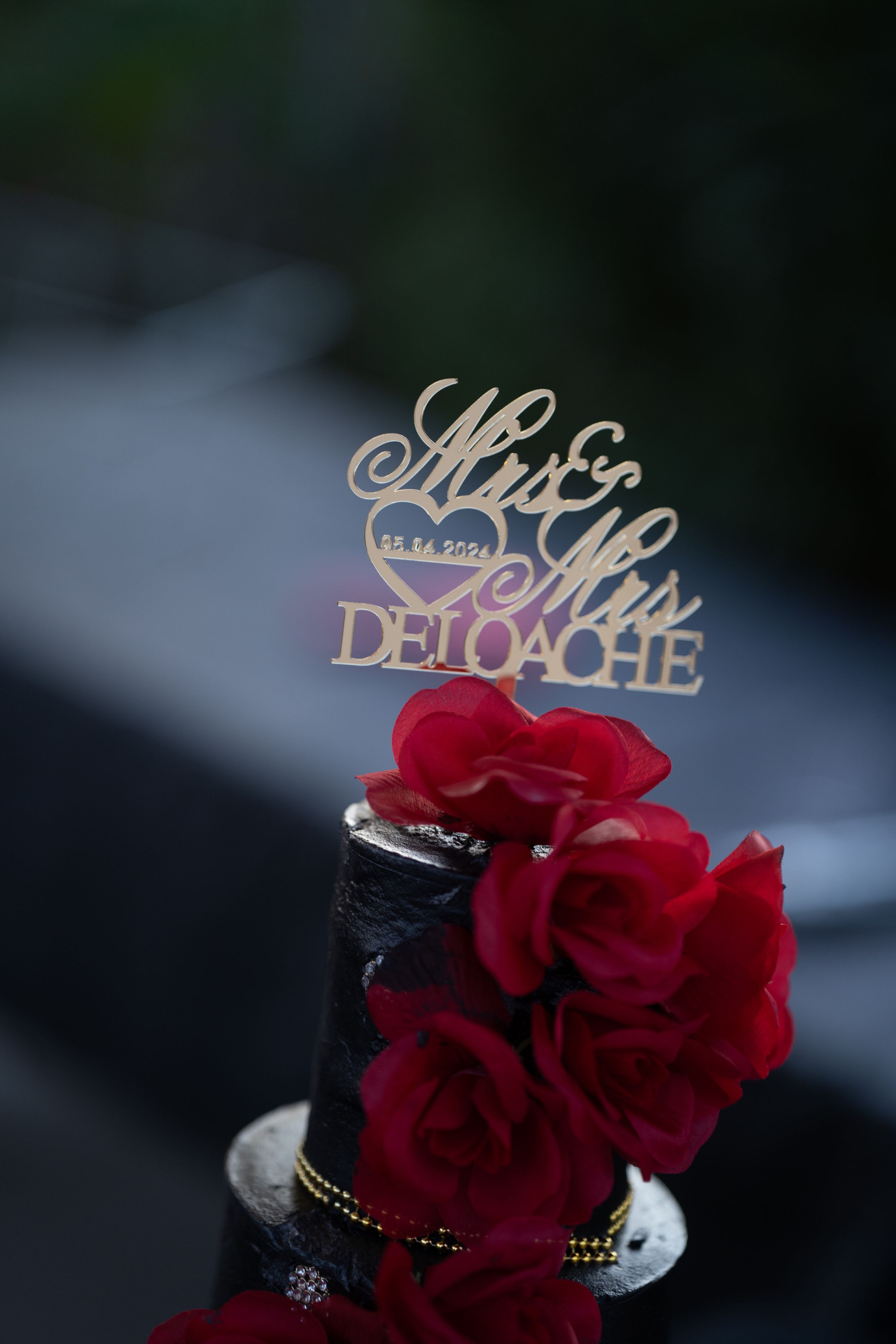 Wedding cake toppers and decorative red roses arranged on a dark background.