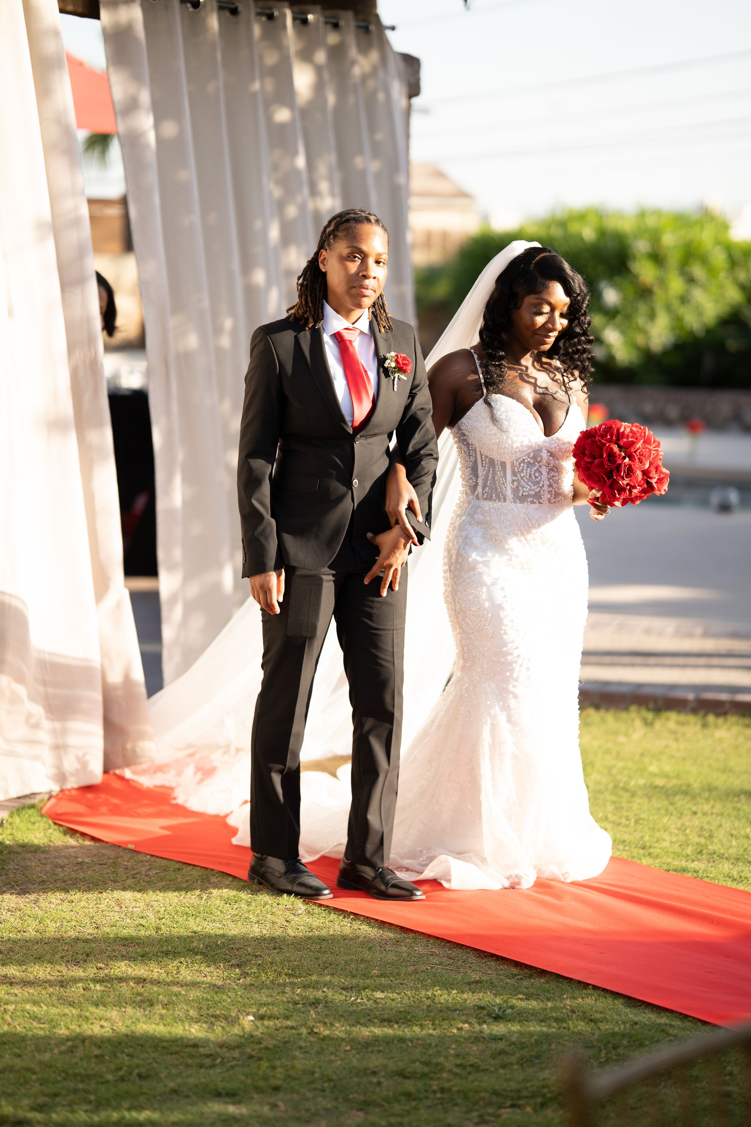 A couple walks down a red carpet path outdoors during their wedding ceremony.