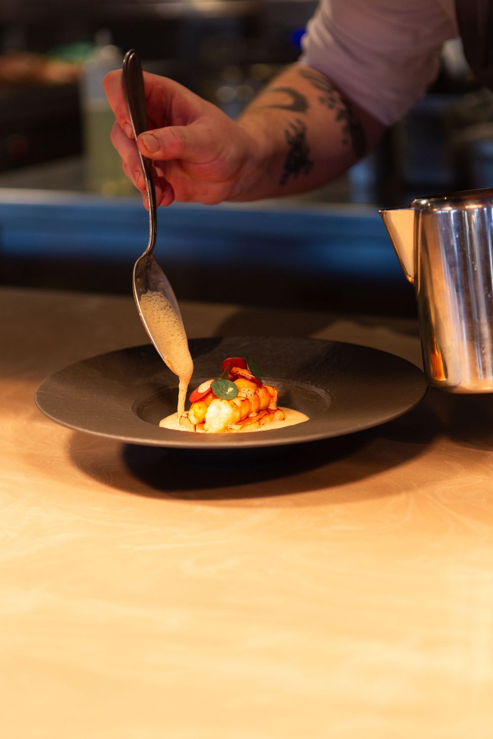 Chef plating delicate portions of food on white plates in a professional kitchen setting.