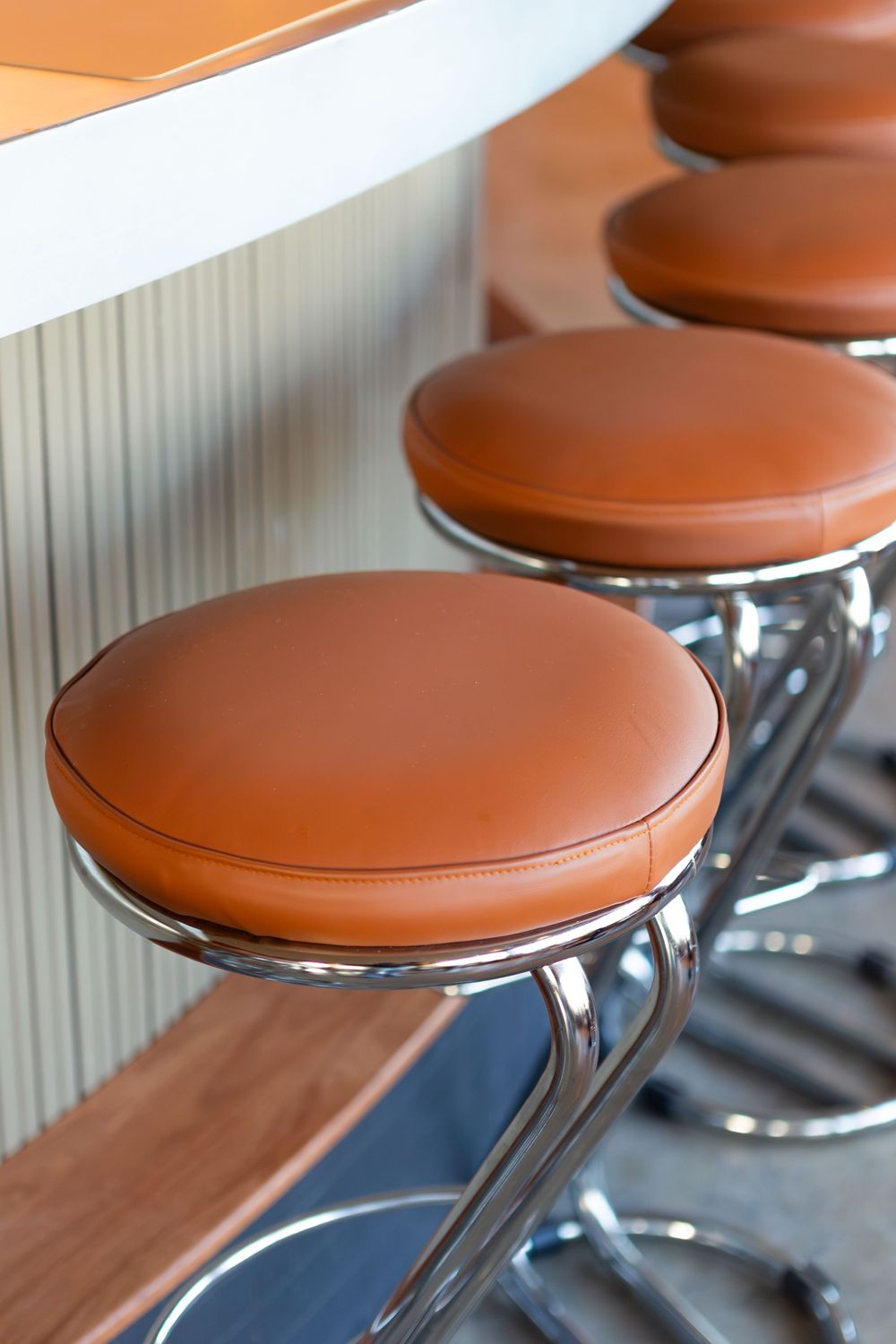 Row of modern brown leather bar stools with chrome bases lined up at a counter.