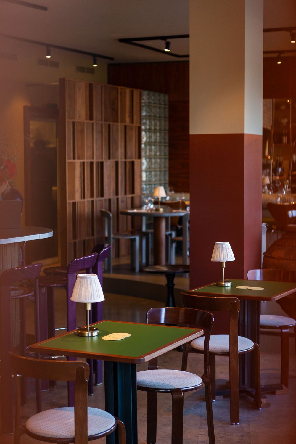 Modern restaurant interior with green-topped tables and white chairs illuminated by stylish pendant lamps.