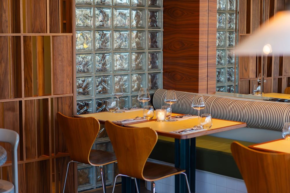 Modern restaurant interior with glass block wall, wooden panels, and intimate table settings with pendant lighting.