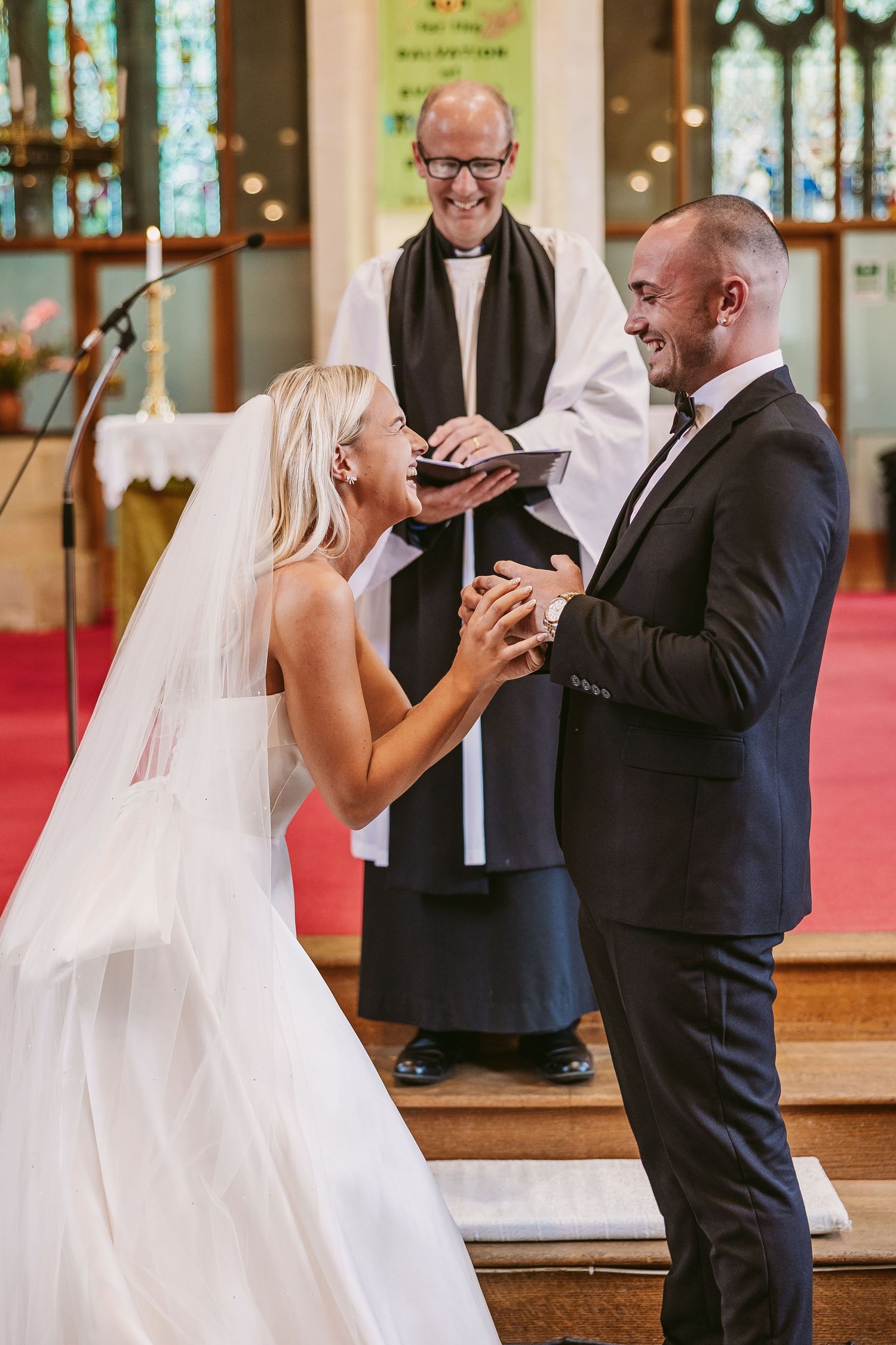 A joyful wedding ceremony moment showing a couple laughing together at the altar with their officiant.