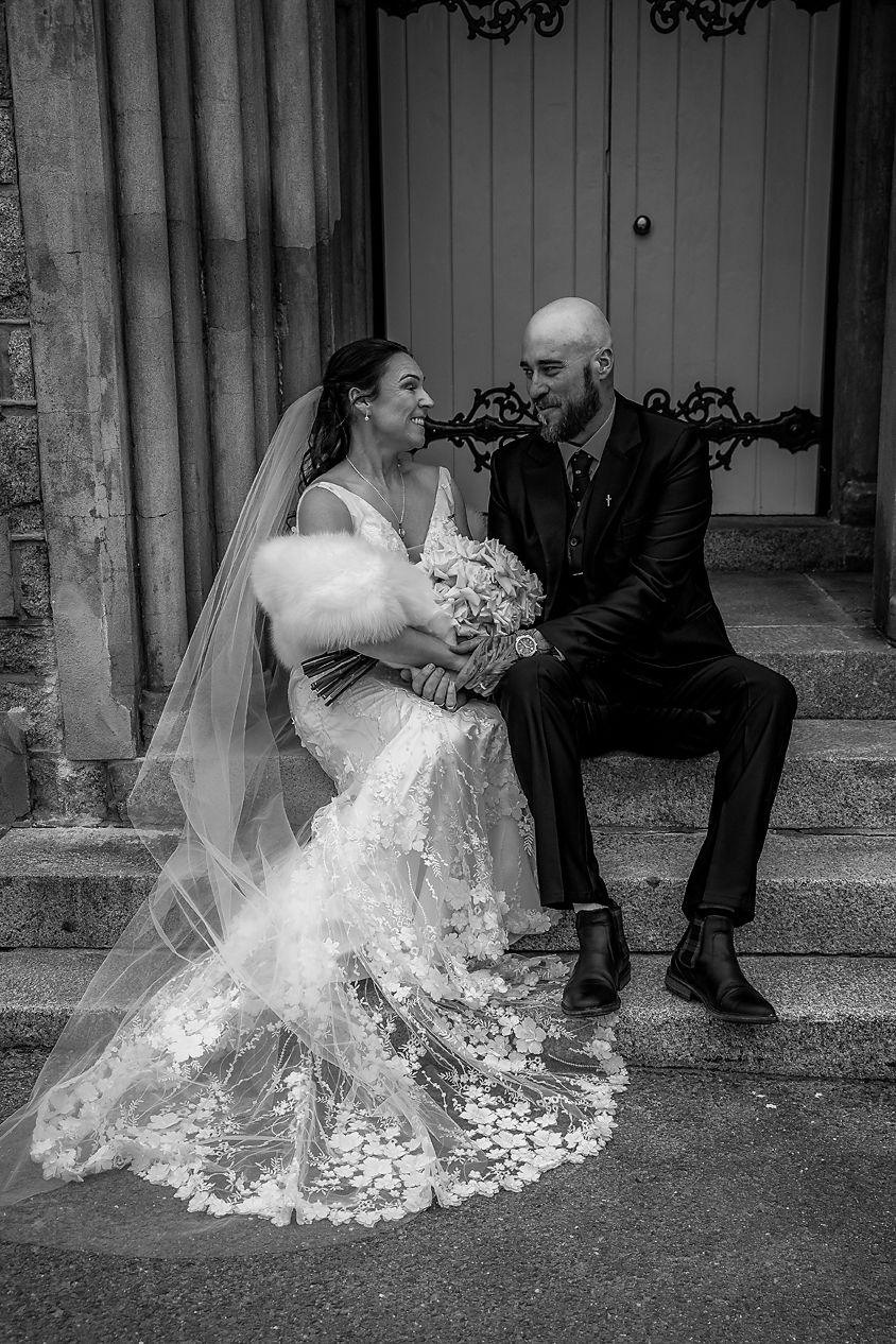 A romantic black and white wedding photo series showing a couple sitting on stone steps with the bride's dress elegantly spread out.