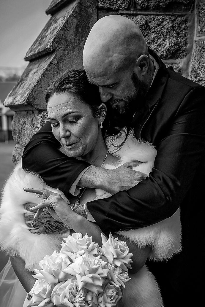 A couple in black embraces and shares intimate moments in a series of black and white photographs with white flowers.