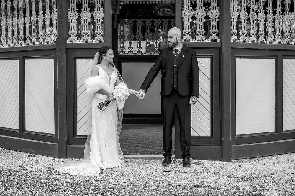A wedding couple and their wedding party pose together on the steps of an ornate building in formal attire.
