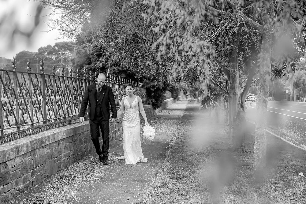 Black and white wedding photos show couple walking along a decorative iron fence in a garden setting.