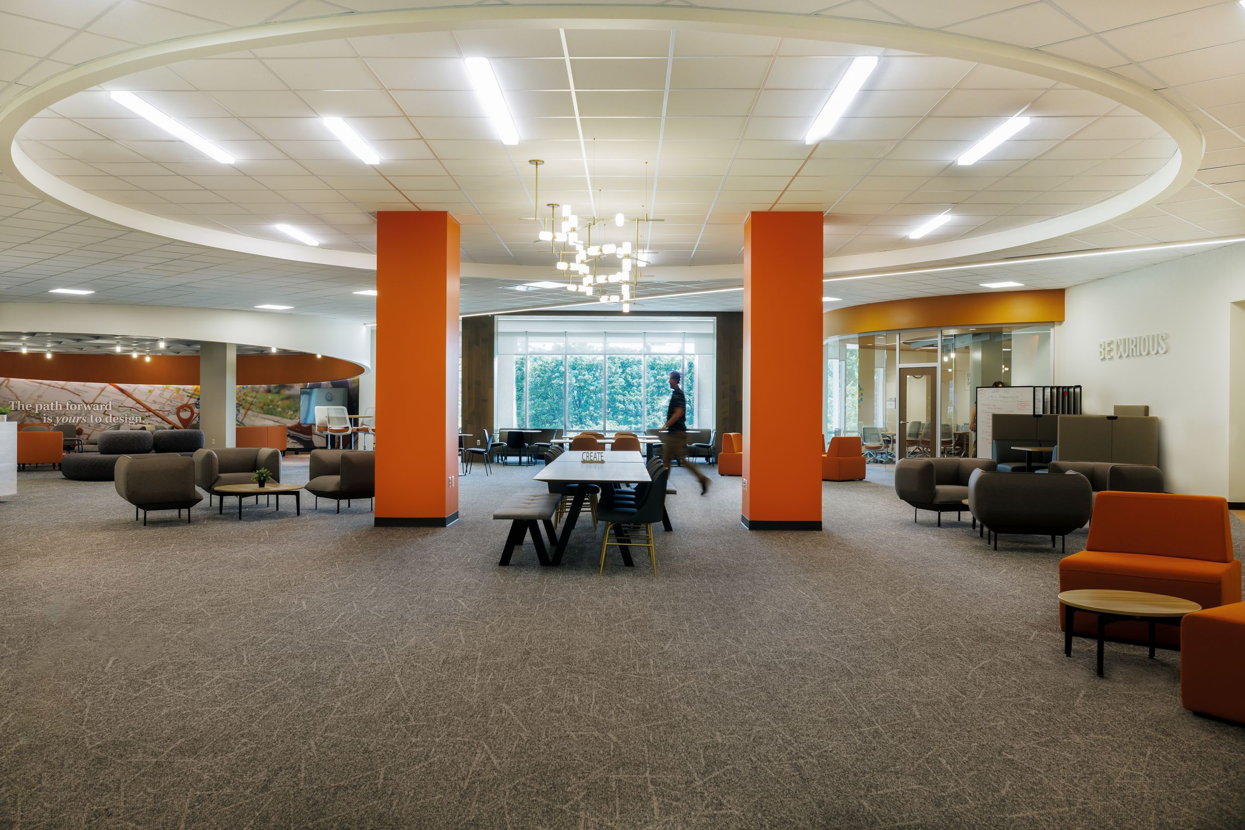 Modern office space with orange pillars, grey carpeting, and contemporary furniture in an open floor plan layout.