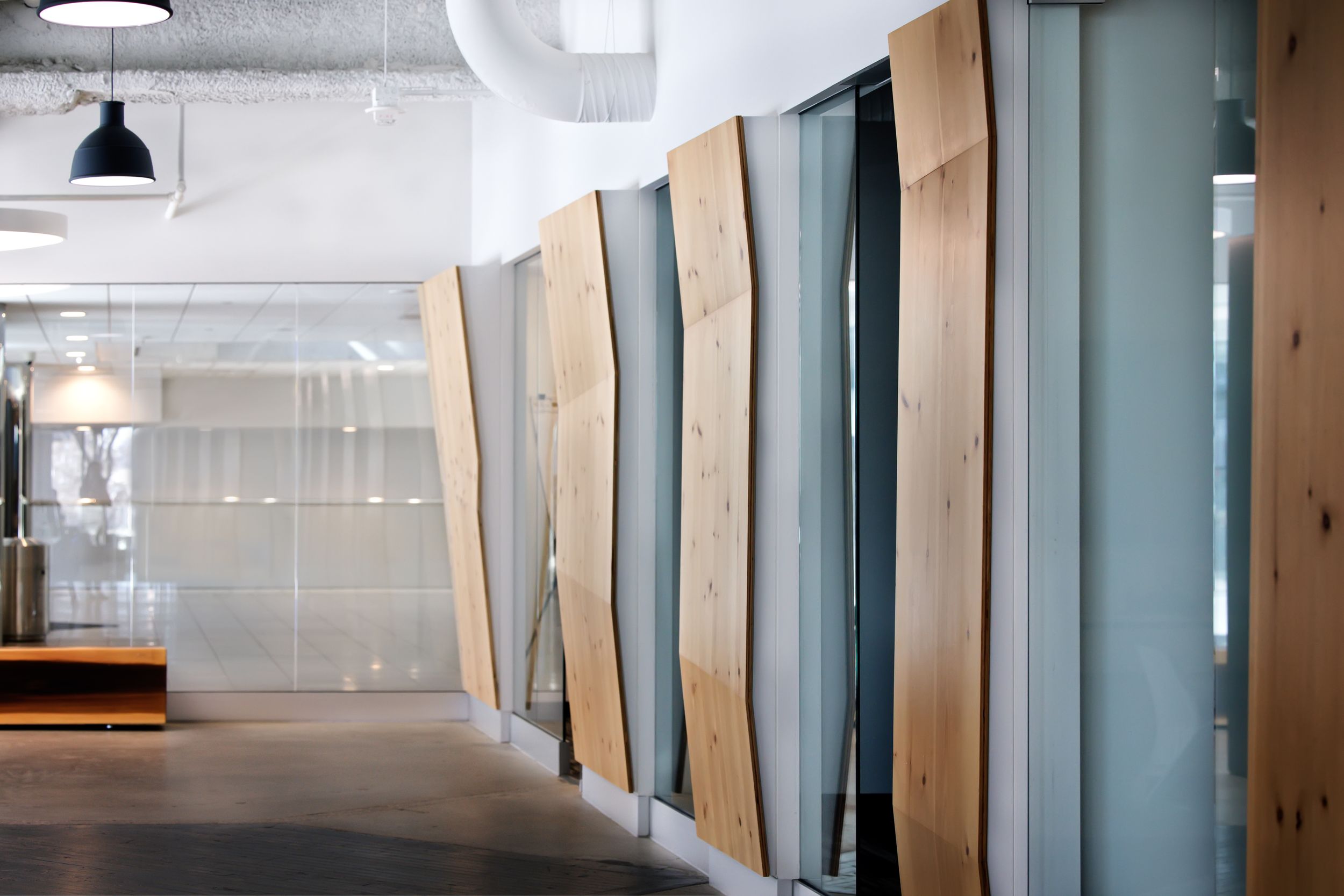 Modern office interior with glass walls, pendant lights, and wooden accents creating a bright minimalist workspace.