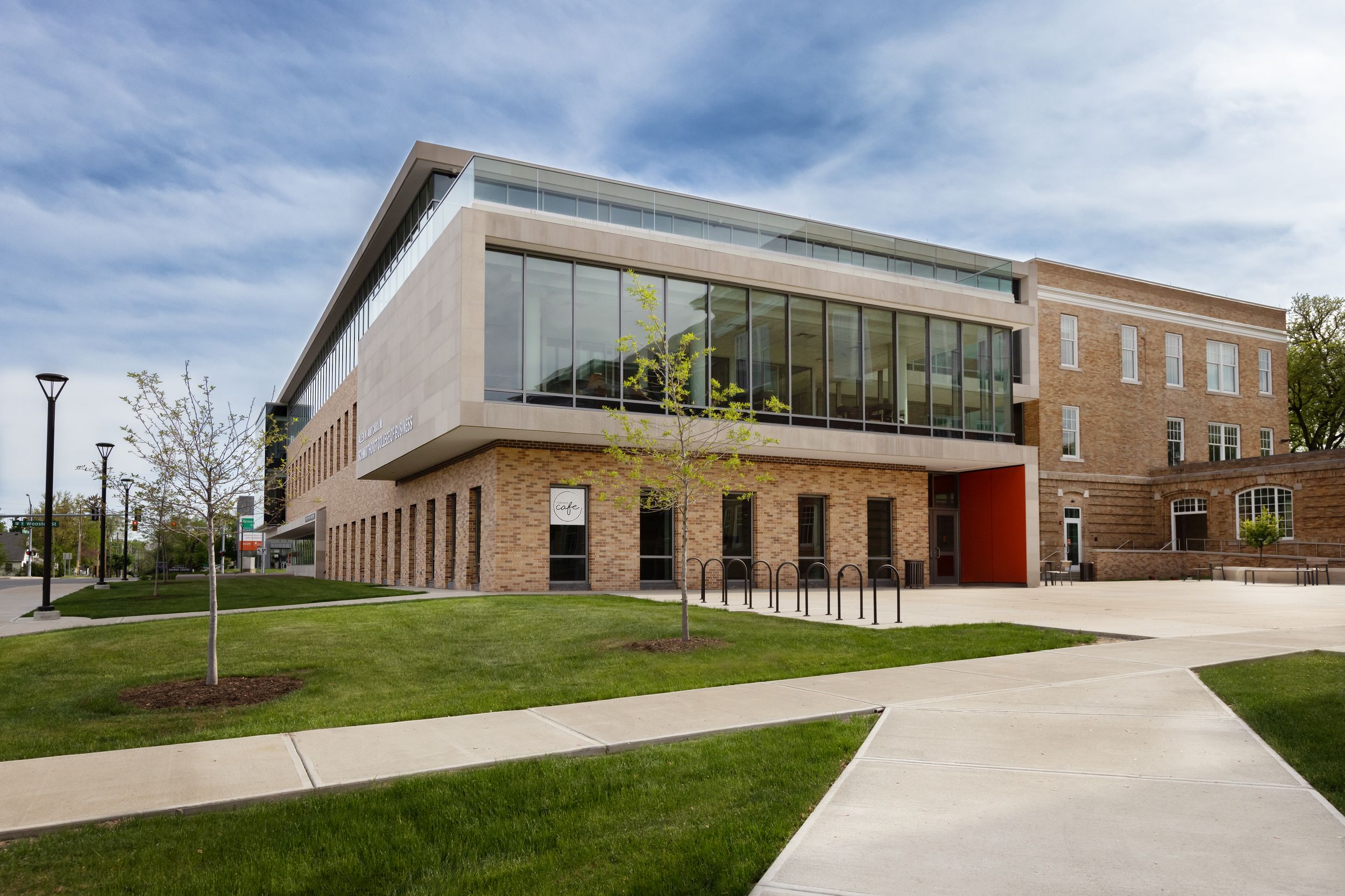 Modern educational facility building exterior with glass walls and brick facade under cloudy blue sky.