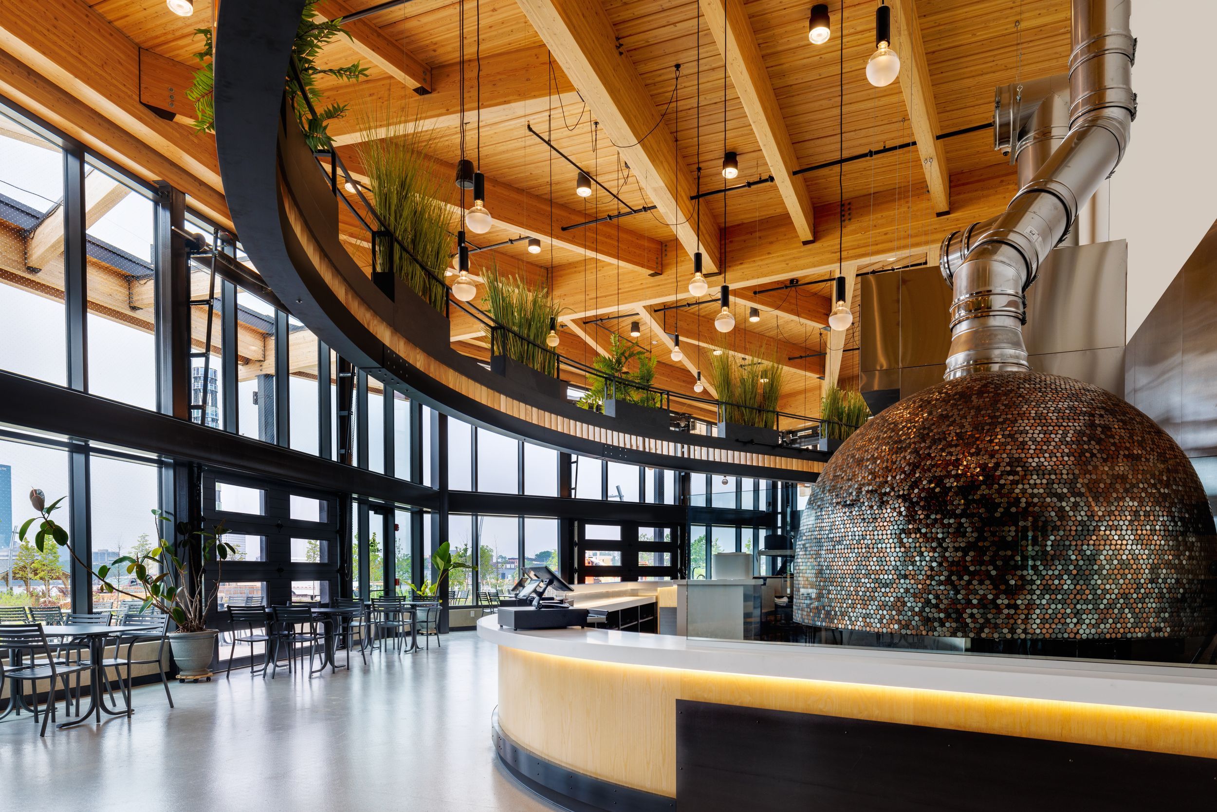 Modern office interior with curved wooden ceiling, large windows, and contemporary lighting fixtures in an open floor plan design.