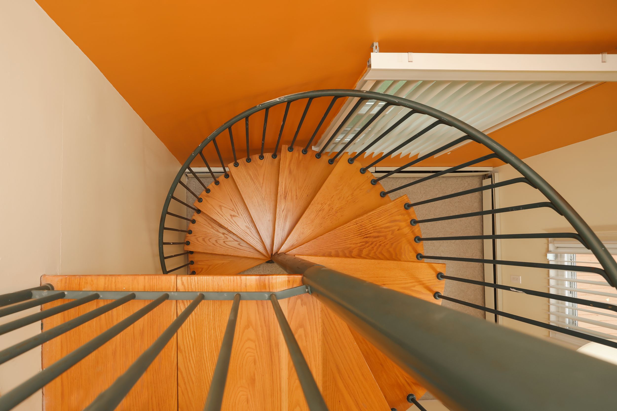 Geometric pattern of orange walls and black metal railings in a modern spiral staircase viewed from below.