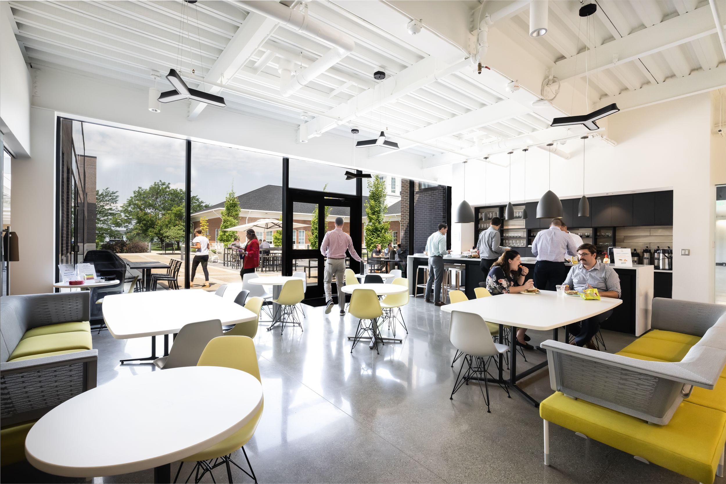 Modern open office space with white tables, yellow accent chairs and exposed industrial ceiling details.
