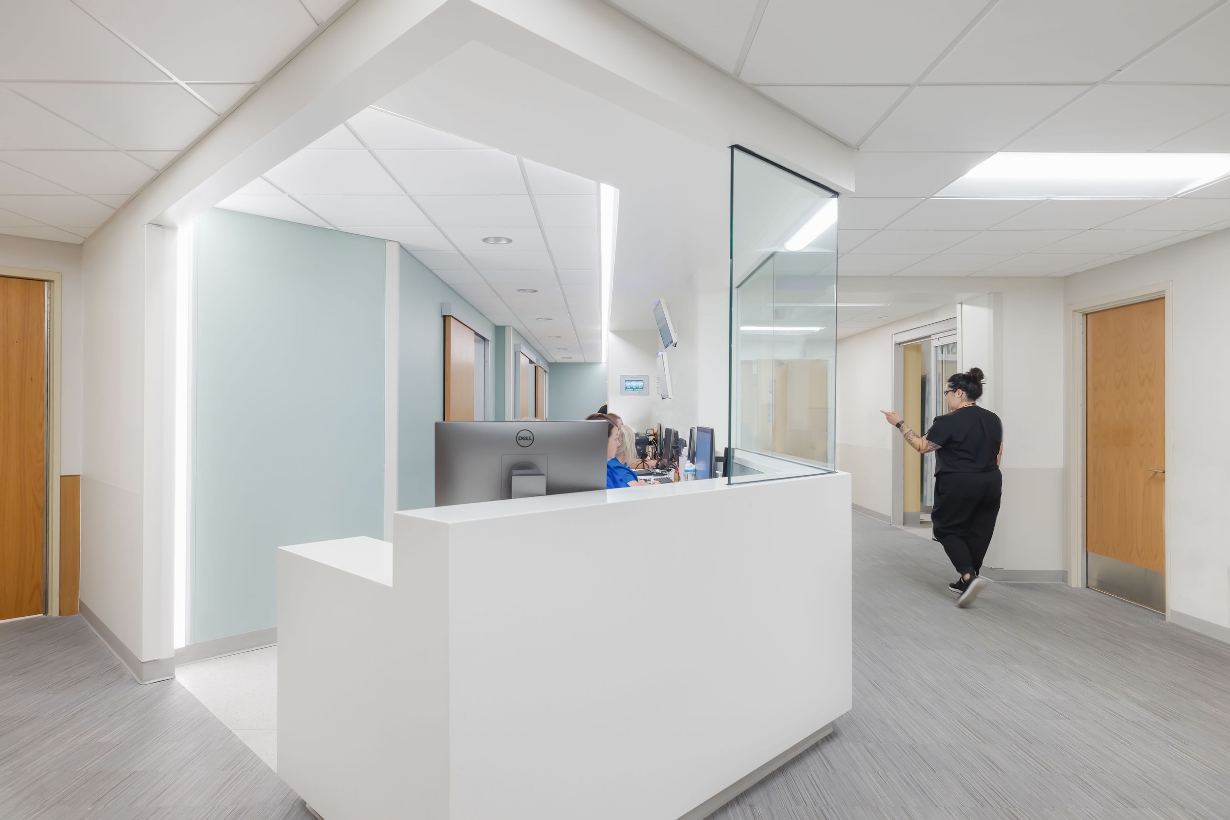 Modern medical office interior with white reception desk, grey flooring, and glass partition in bright clinical setting.