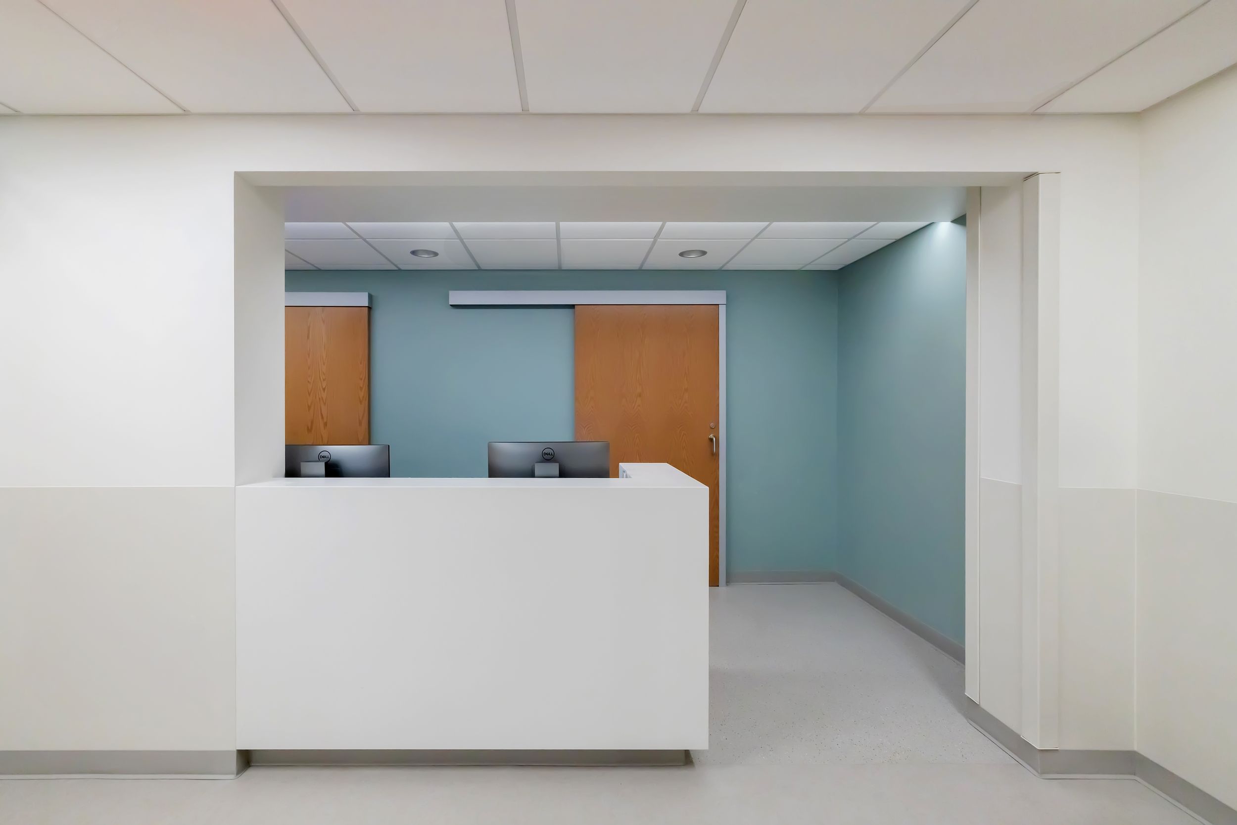 Modern office hallway with white walls, teal accent wall, and recessed lighting creating a clean professional environment.