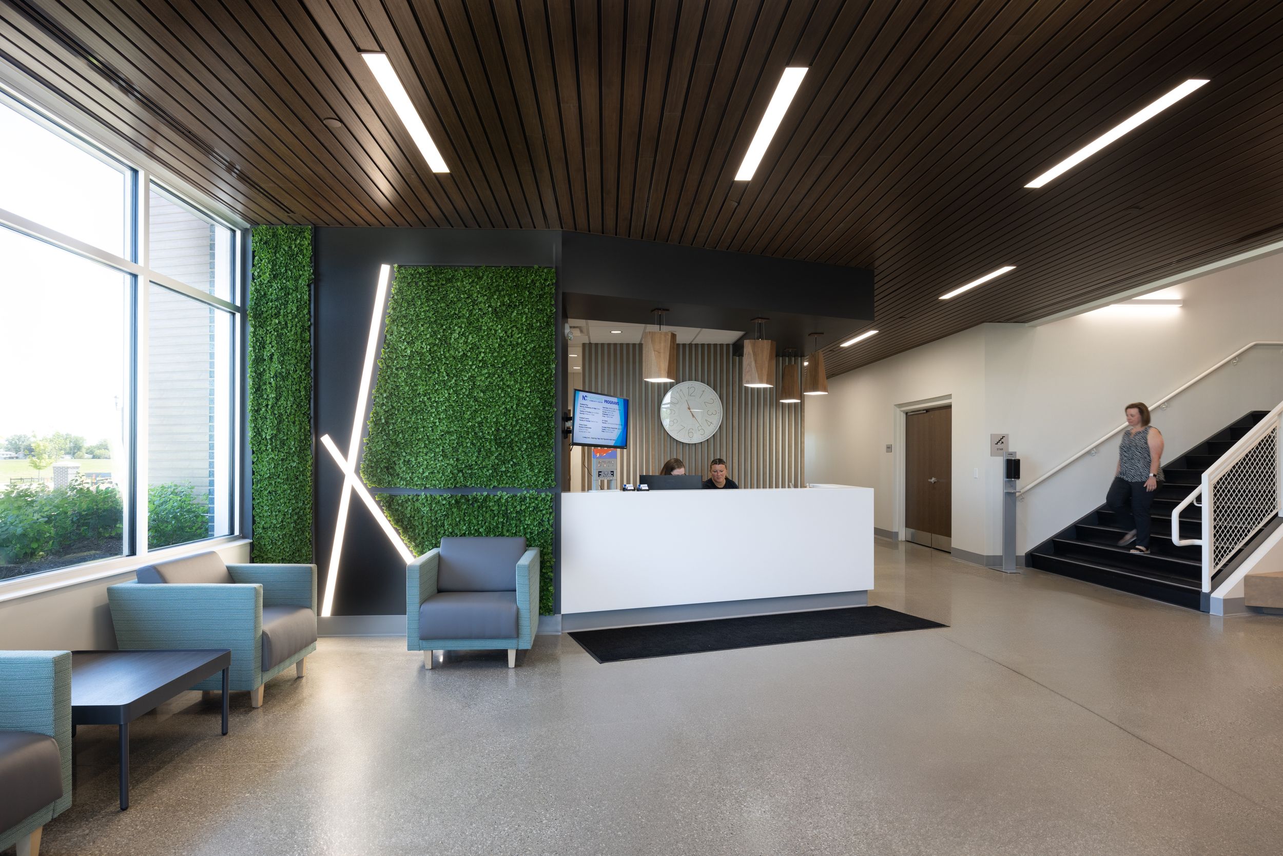 Modern office hallway with wood ceiling panels, linear lighting, and green living wall features along one side.