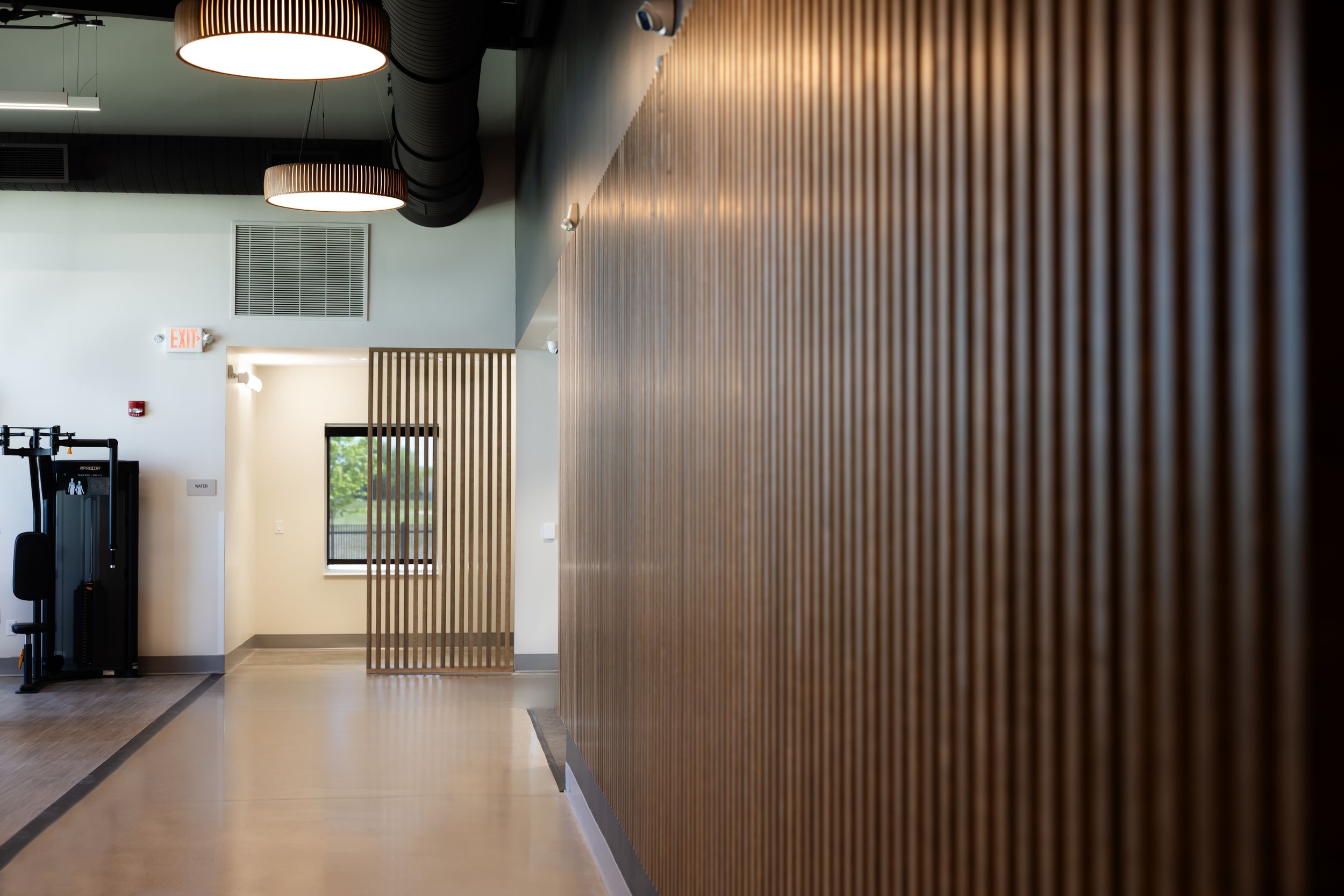 Modern office hallway with wood slat walls, pendant lighting, and polished concrete floors creates a sleek corporate environment.
