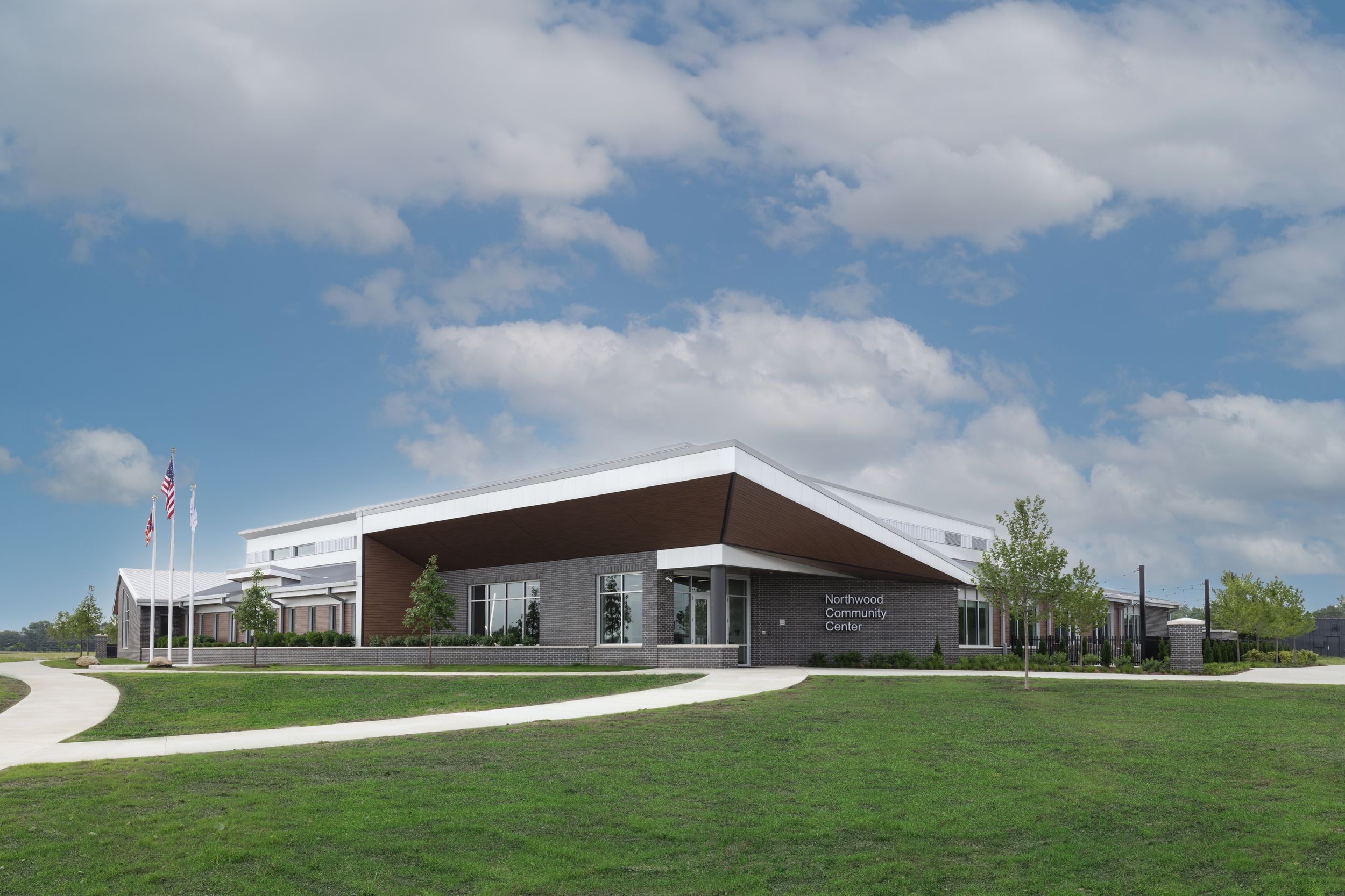 A panoramic view of a modern building complex with green lawns and blue sky with scattered white clouds.