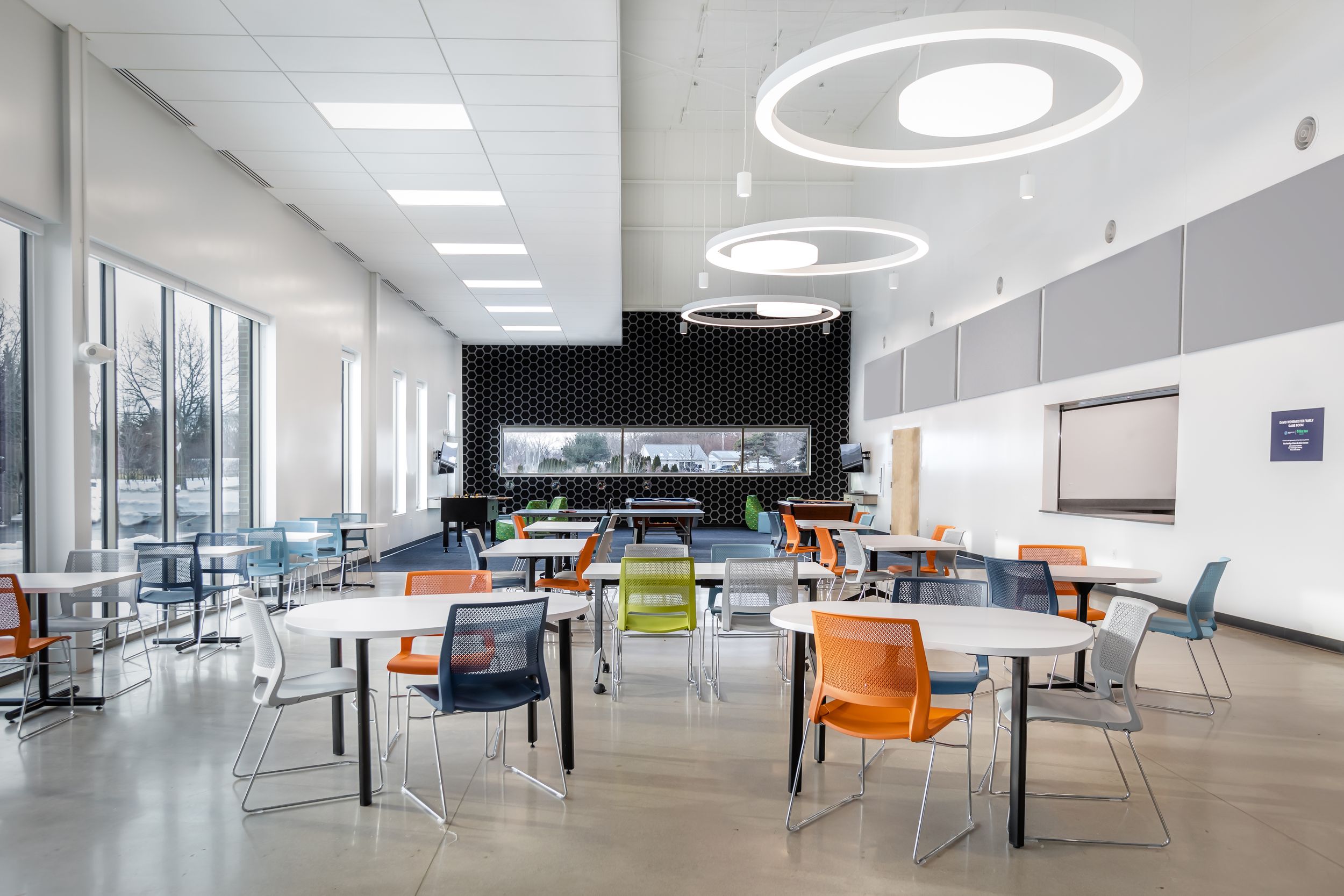 Modern office interior with white ceiling, fluorescent lighting and colorful furniture arranged in an open workspace layout.