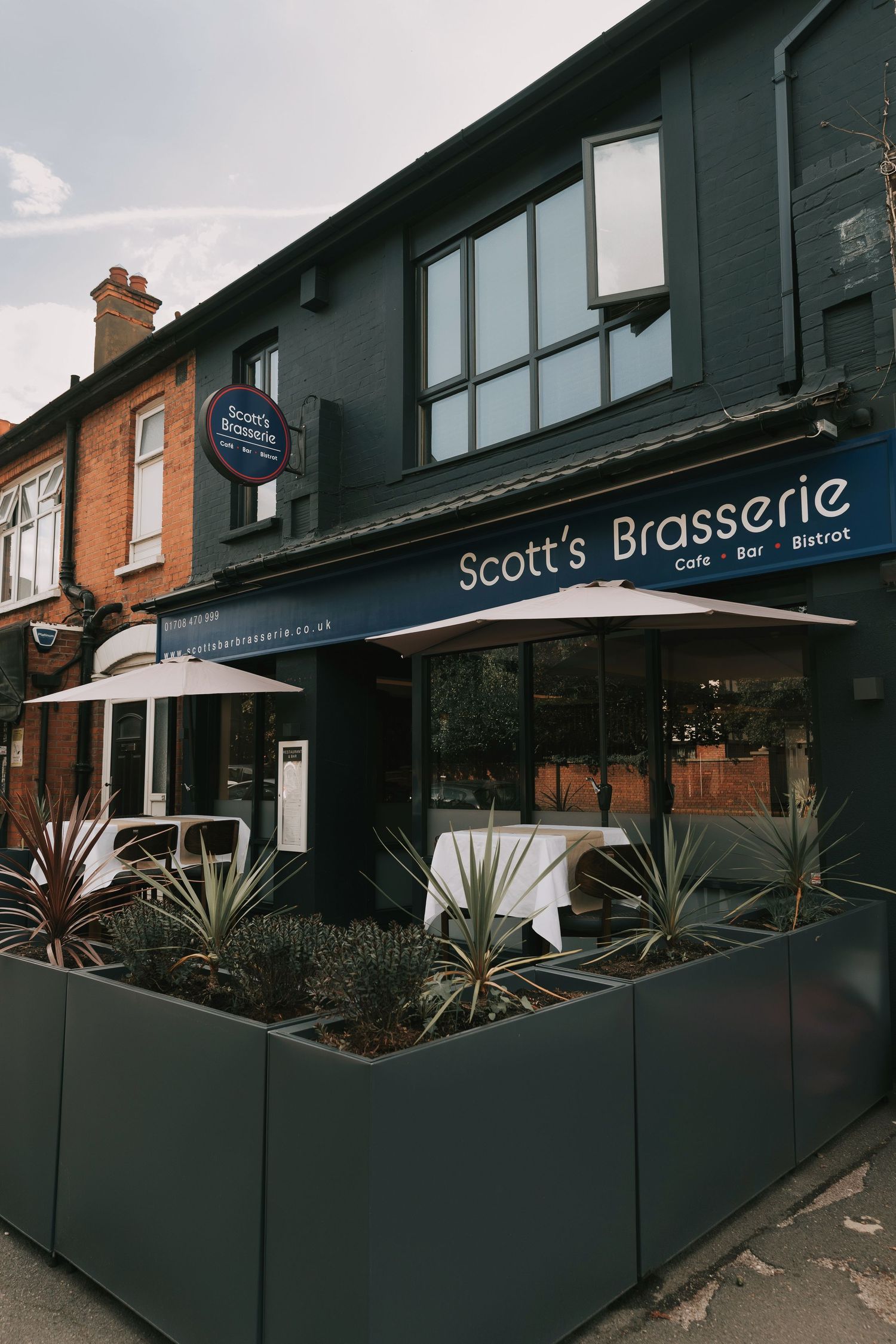 Exterior view of Scott's Brasserie restaurant with modern dark fencing and tropical plants along the outdoor seating area.