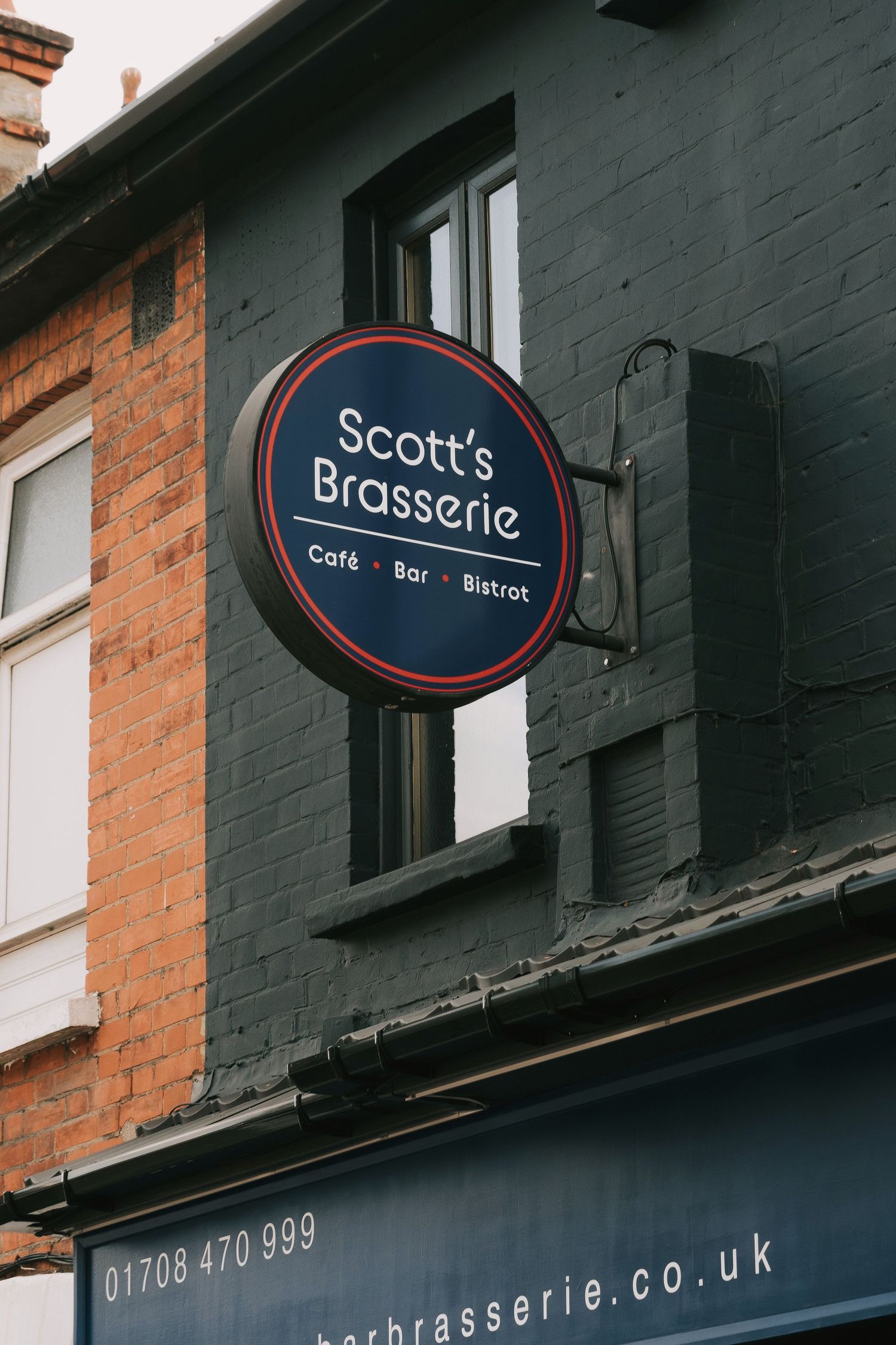 Exterior storefront signs for Scott's Brasserie restaurant with navy blue circular signage mounted on brick building.
