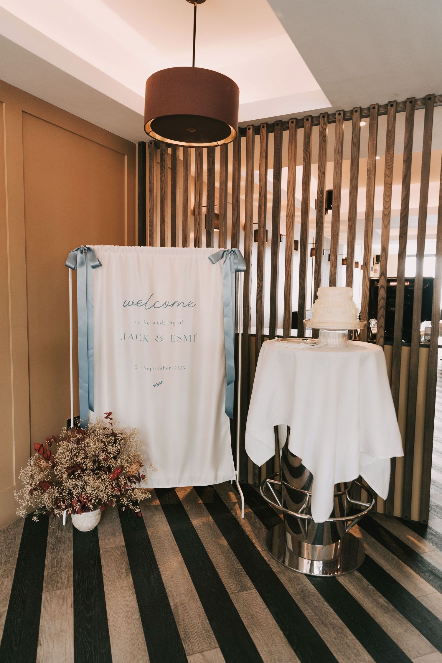 White welcome signs and floral arrangements displayed on wooden slat wall for wedding decor.