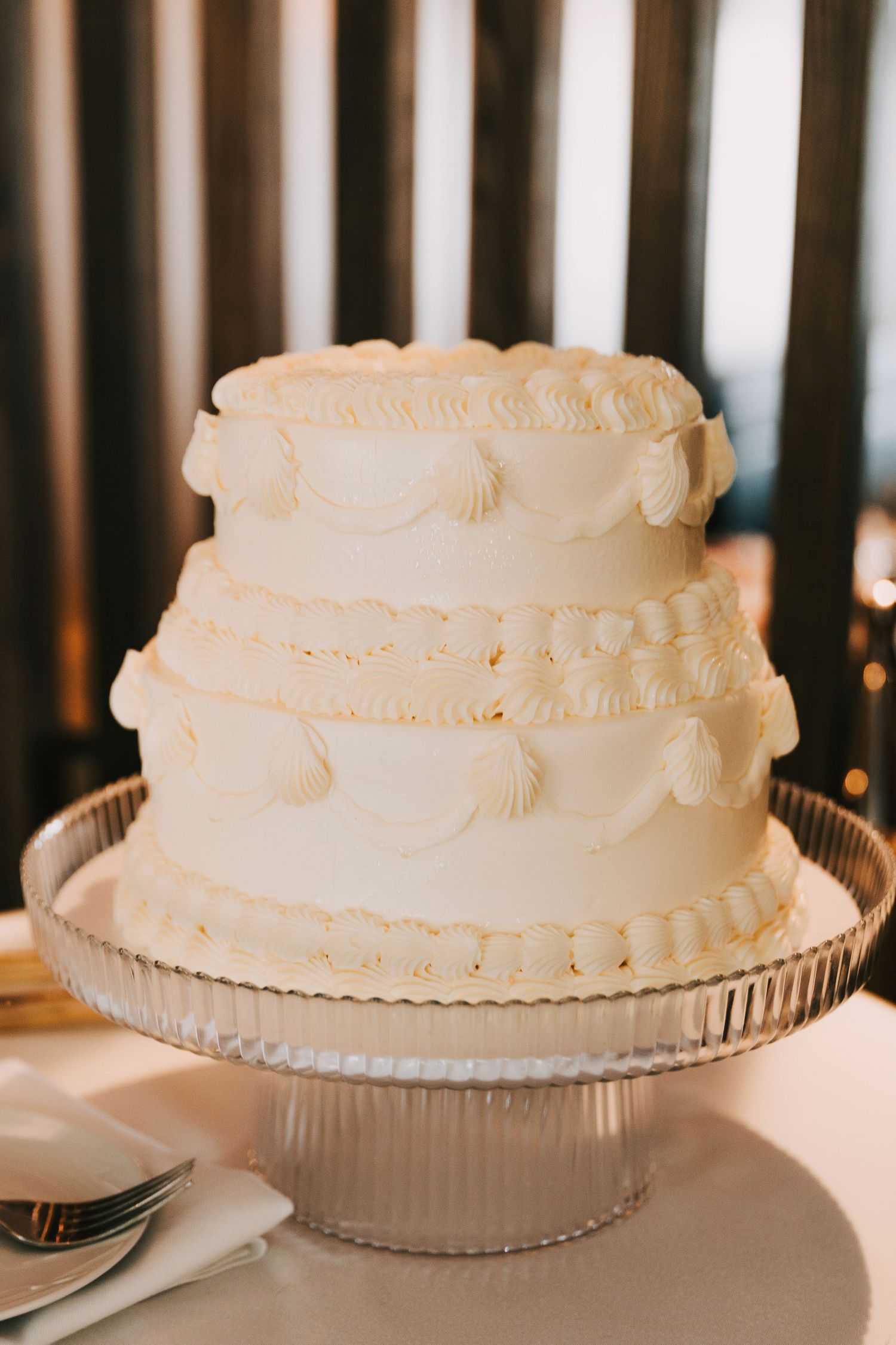 Three elegant white wedding cakes with delicate piping details displayed on silver cake stands.