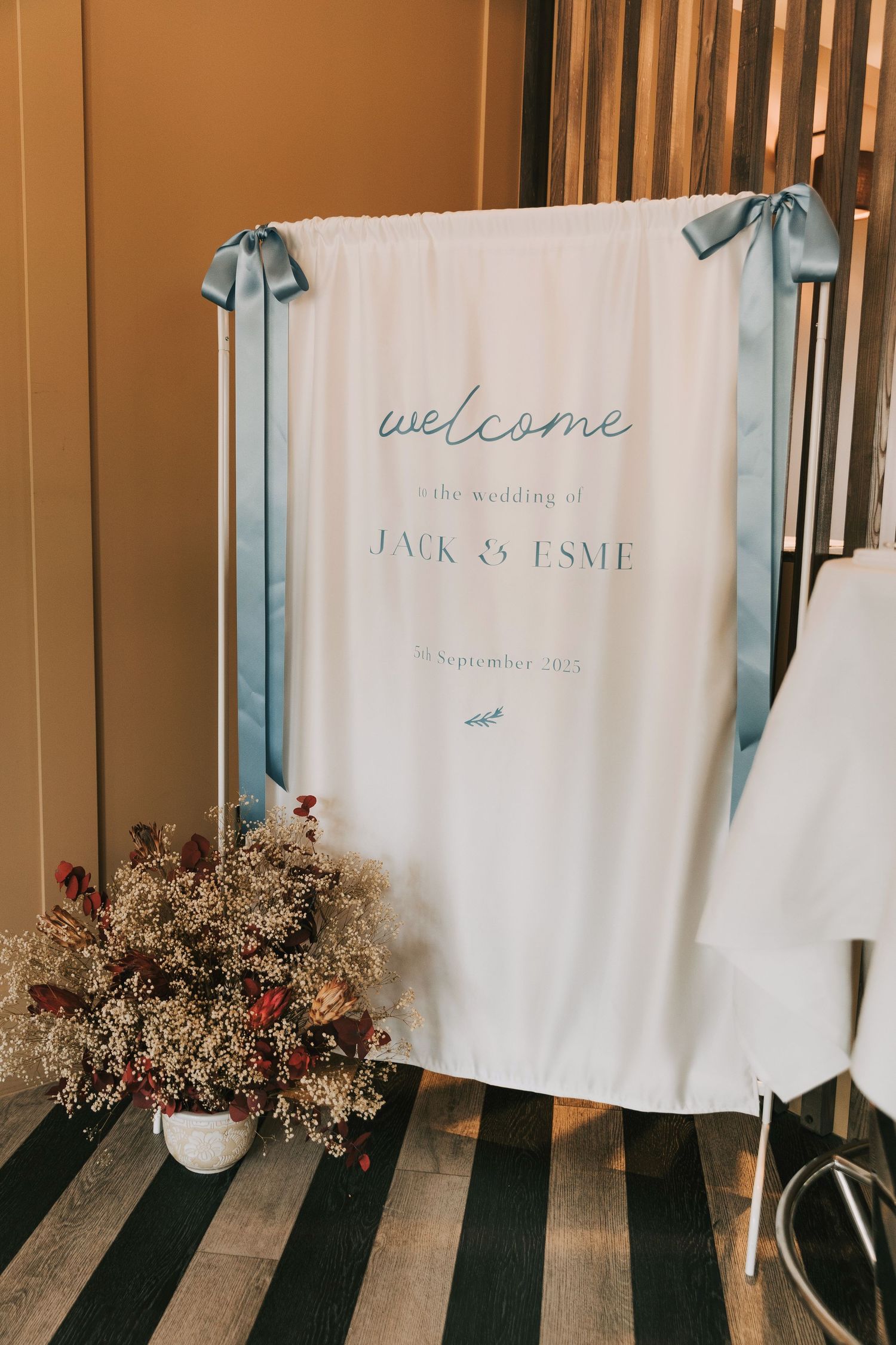White fabric wedding backdrop with floral decorations and text against a wooden wall.