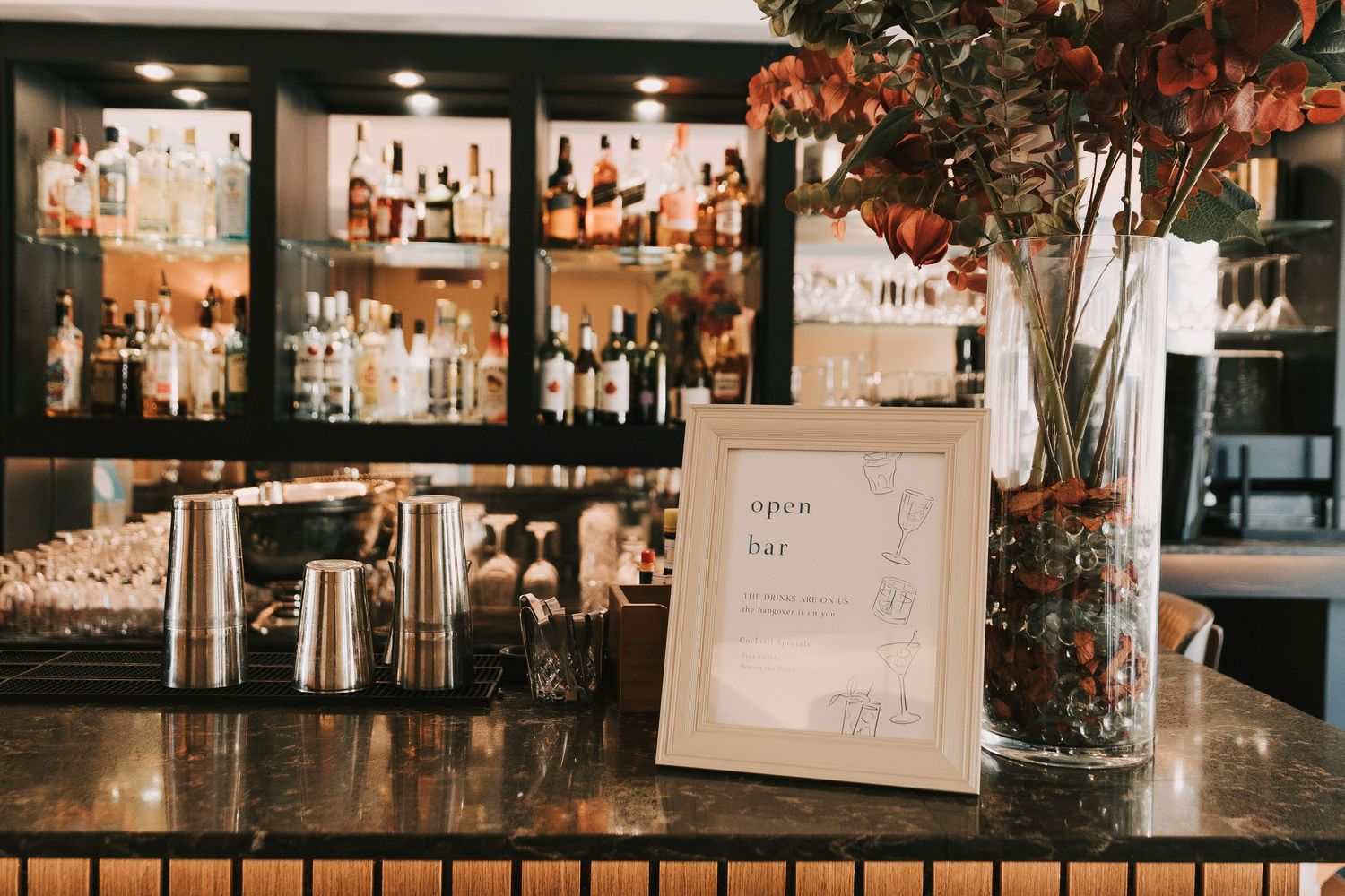 Interior bar view showing illuminated shelves of liquor bottles and glassware in warm lighting.