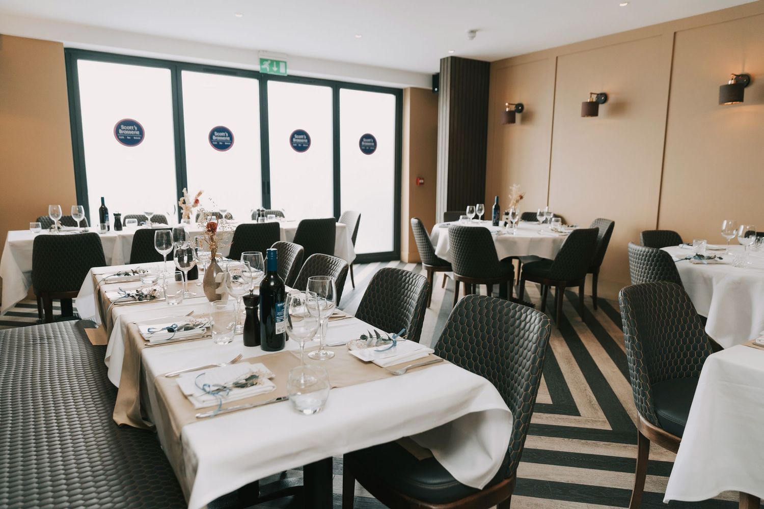 Elegant restaurant interior with white tablecloths, dark chairs and geometric window panels in an upscale dining room.