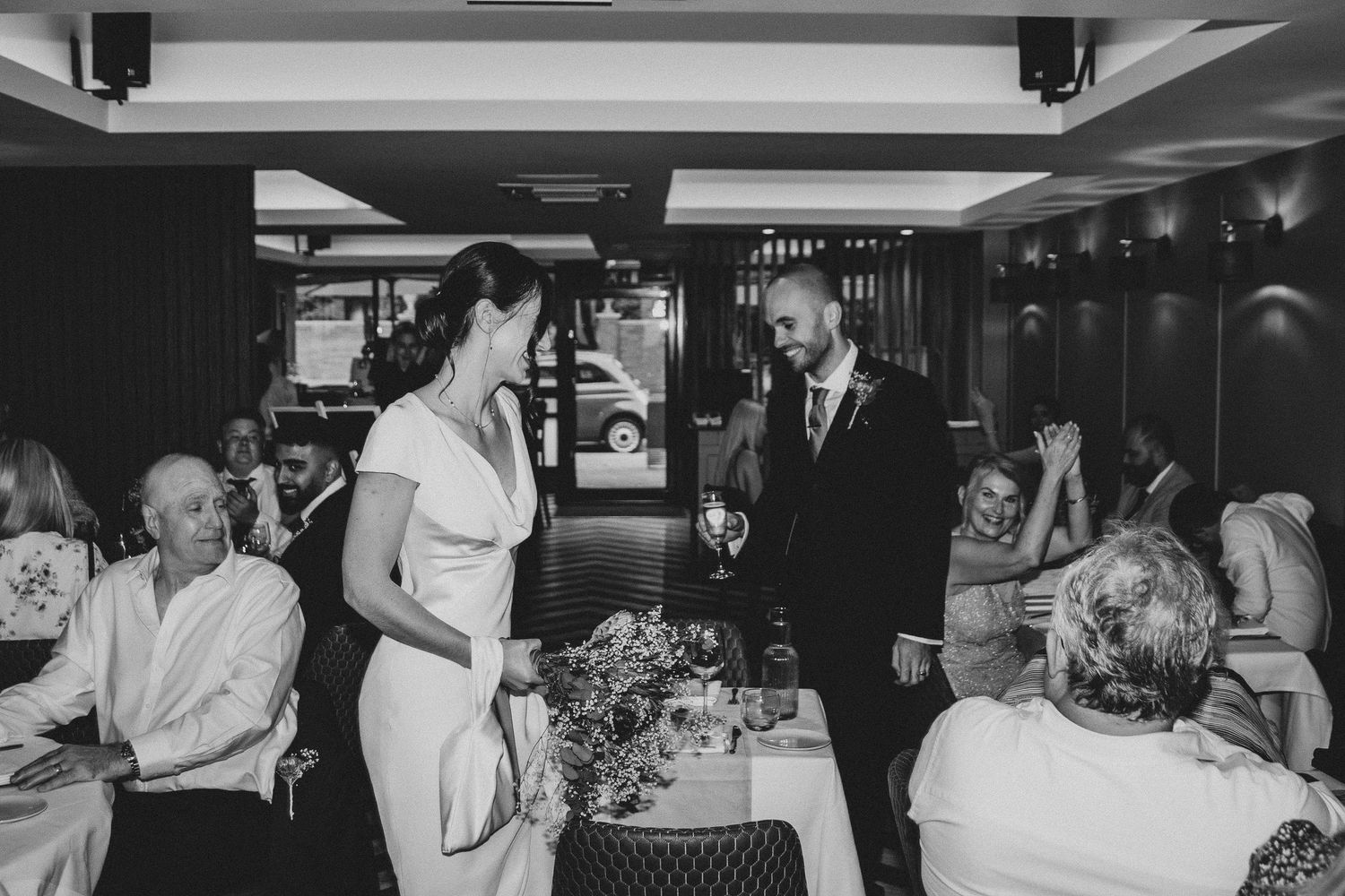 Black and white photos of wedding reception showing dining tables and guests celebrating in an indoor venue.
