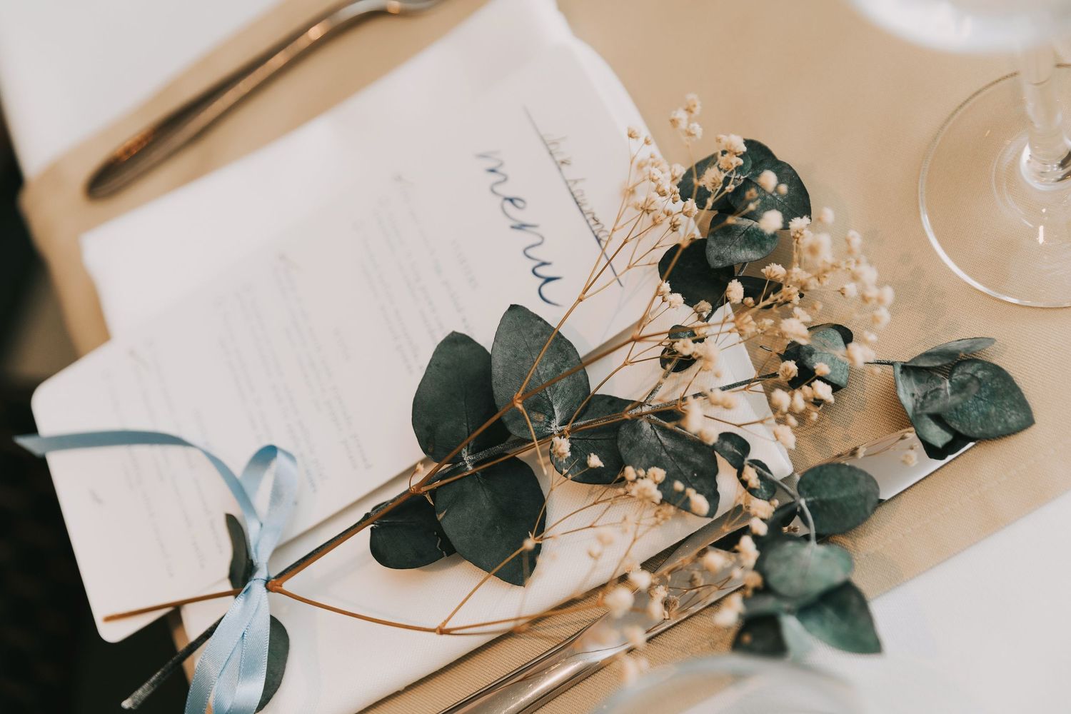 Wedding table decor with delicate eucalyptus leaves and white floral arrangements on neutral beige tablecloths.