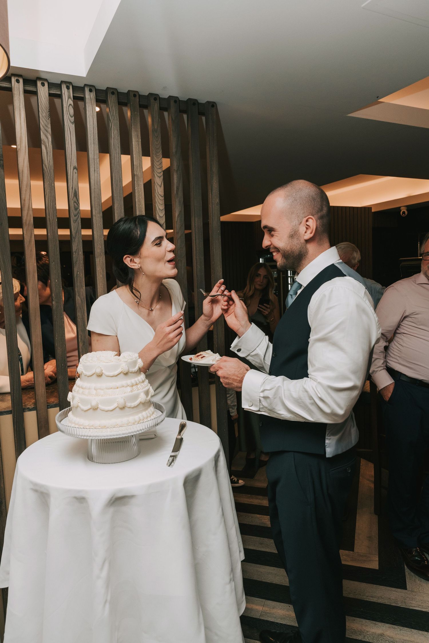 Candid moments of wedding party members enjoying cake and laughter at an indoor reception.
