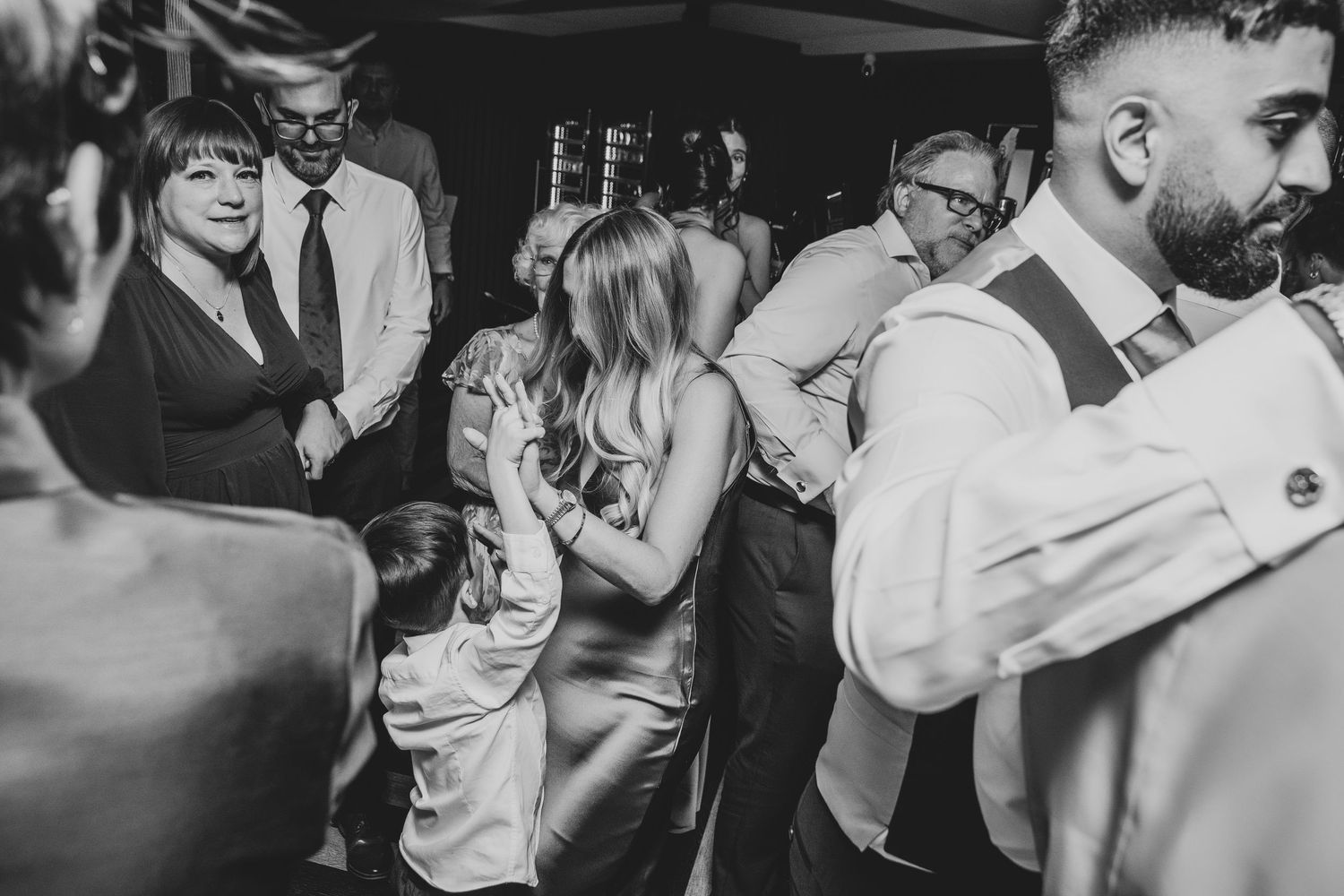 Monochrome image of couples dancing and embracing on a dimly lit dance floor.