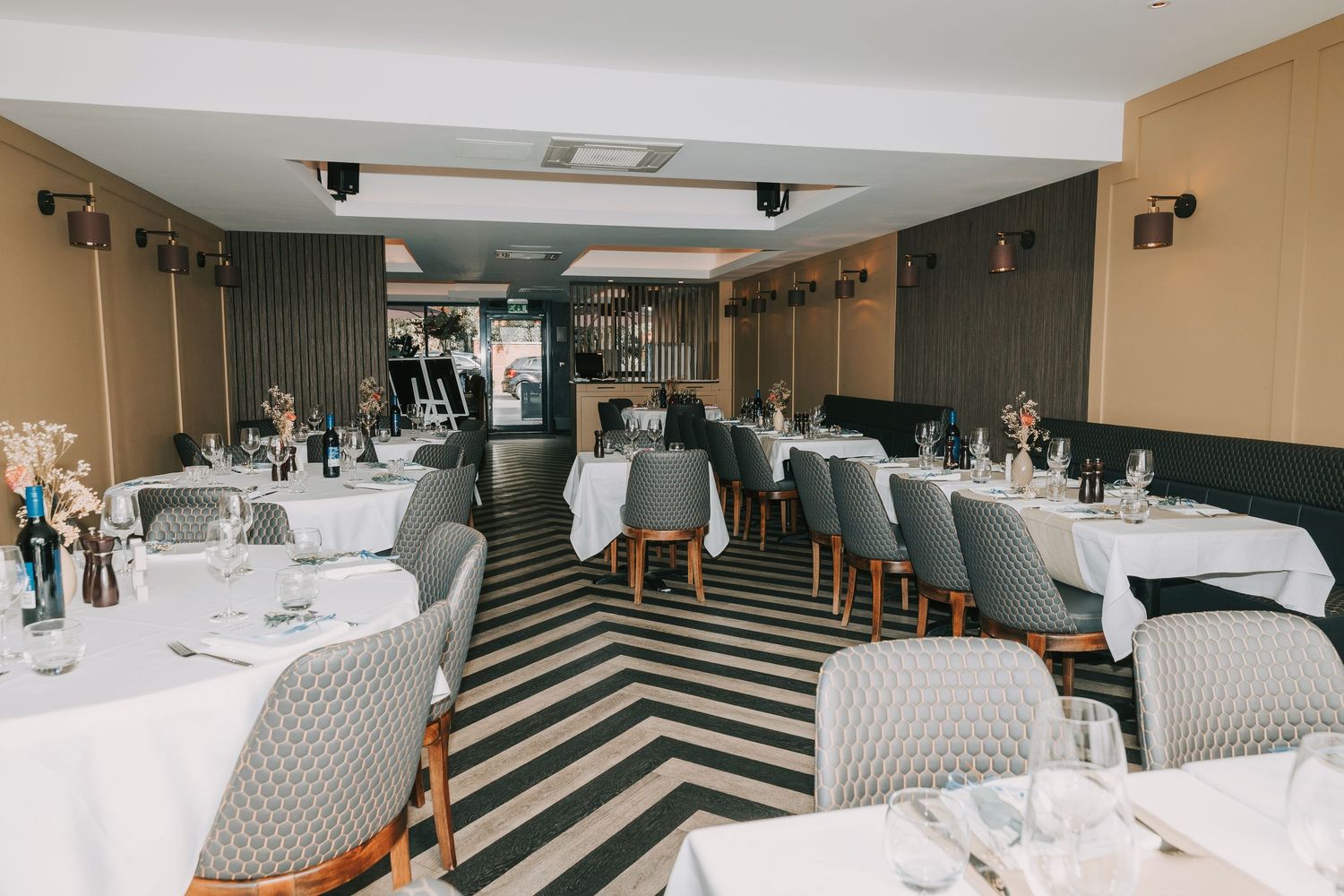 Modern restaurant interior with geometric floor patterns and white dining tables arranged in a panoramic view.
