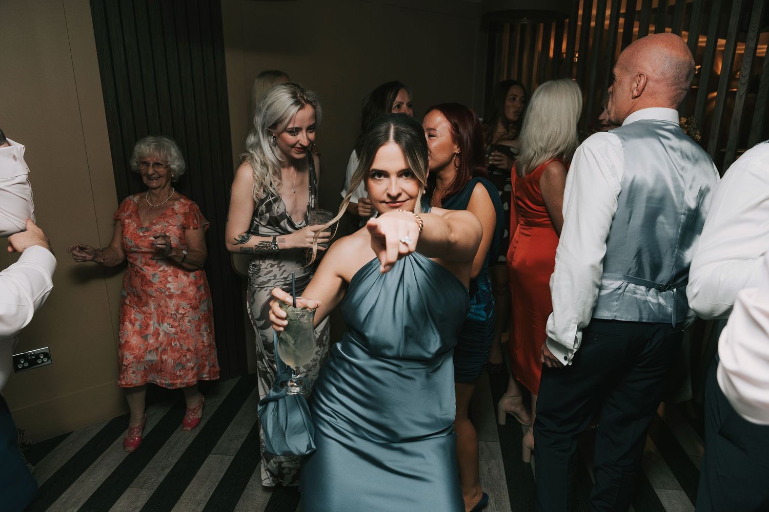 People dancing and socializing at a dimly lit indoor wedding party or celebration.