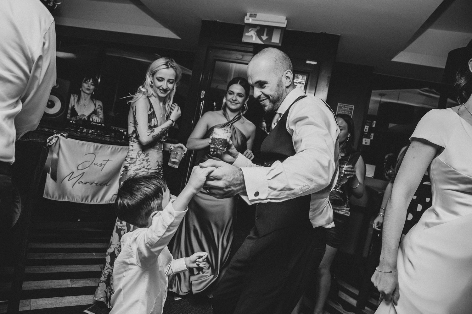 Black and white shot of wedding guests dancing and celebrating in a dark indoor venue.