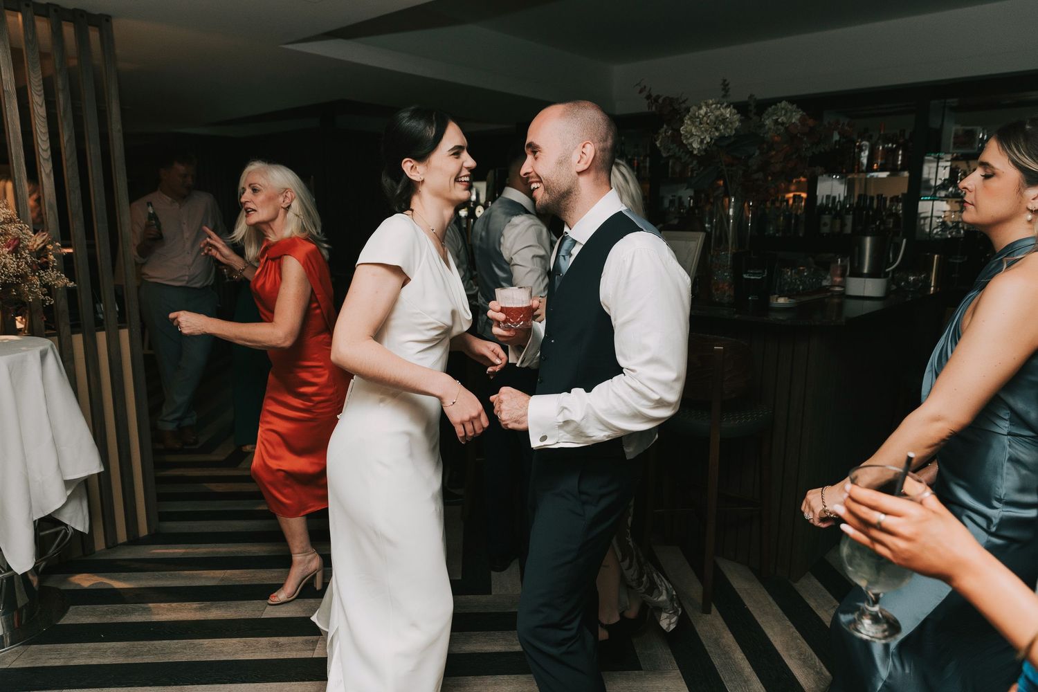 A couple shares a romantic moment while dancing together at a wedding reception with other guests in the background.