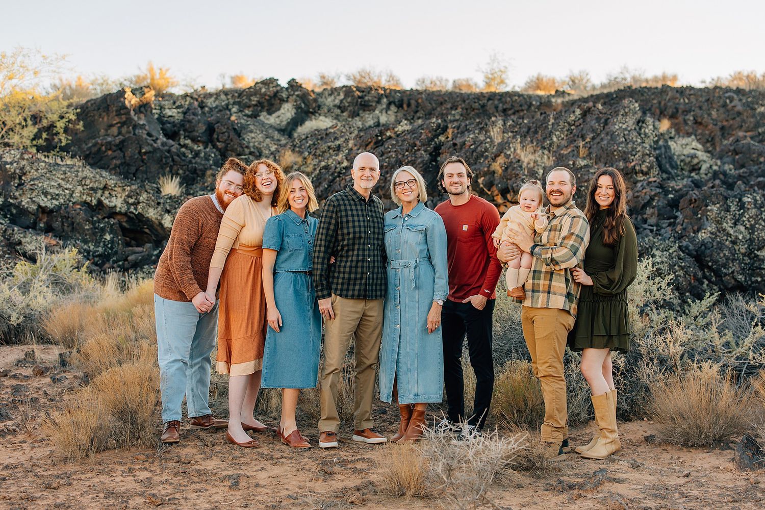 Group of people wearing coordinated earth-toned outfits pose together on rocky desert terrain at sunset.