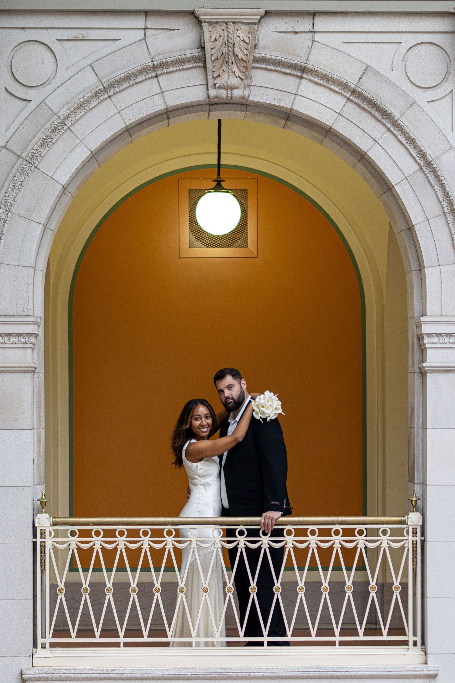 Three connected arched balconies with white railings show a romantic wedding couple embracing in golden light.