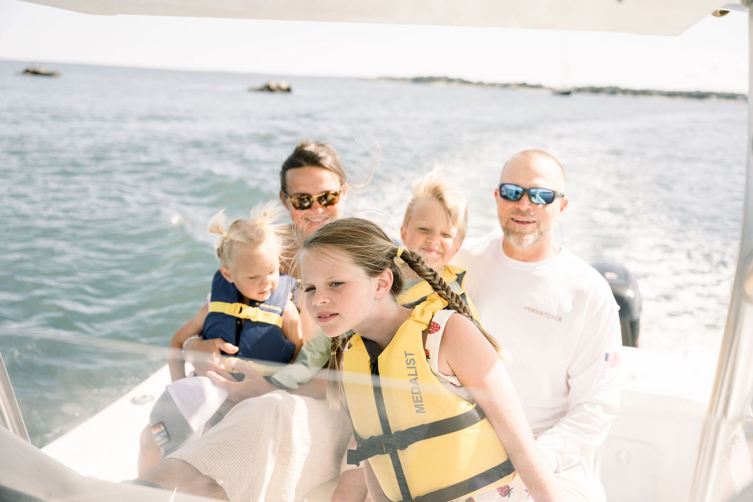 Group of people wearing life jackets enjoy a boat ride on sunny day at sea.