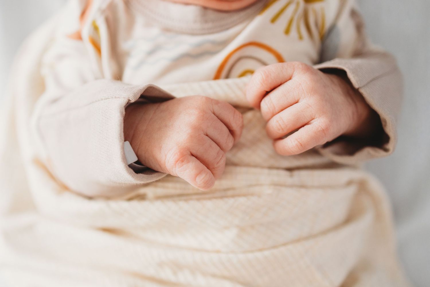 Tiny baby feet and toes peek out from under a soft cream-colored blanket or swaddle.