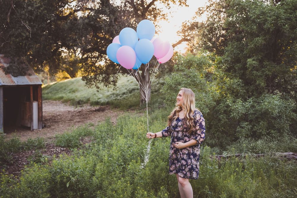 A couple stands in a sunlit forest clearing with colorful balloons during a romantic photo session.