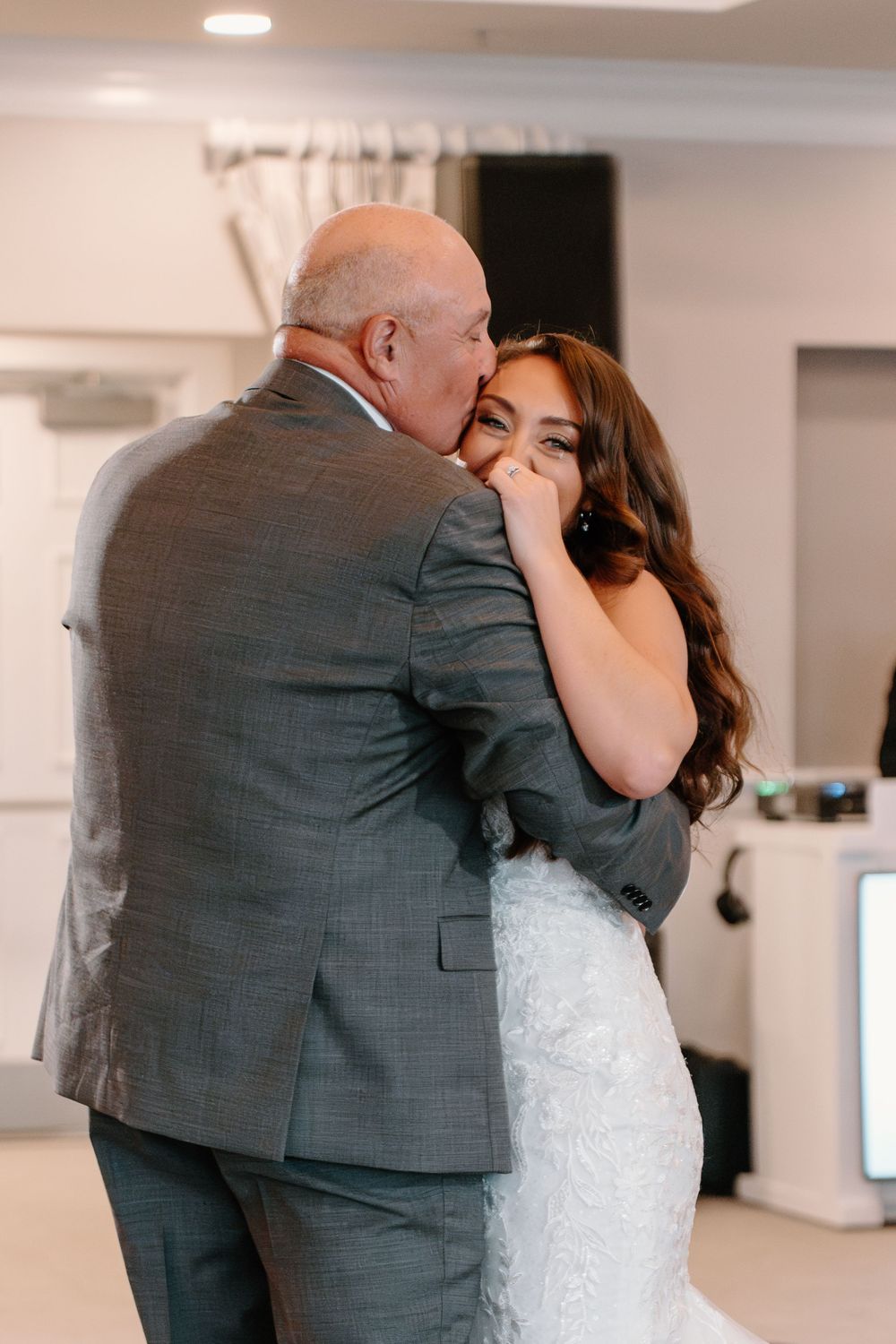 Emotional wedding scene showing a father-daughter dance in a bright indoor venue with tender embraces.