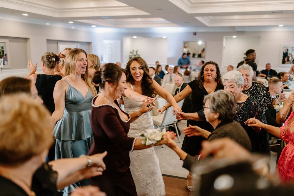 A lively group of wedding guests dancing and celebrating together in a bright reception hall.